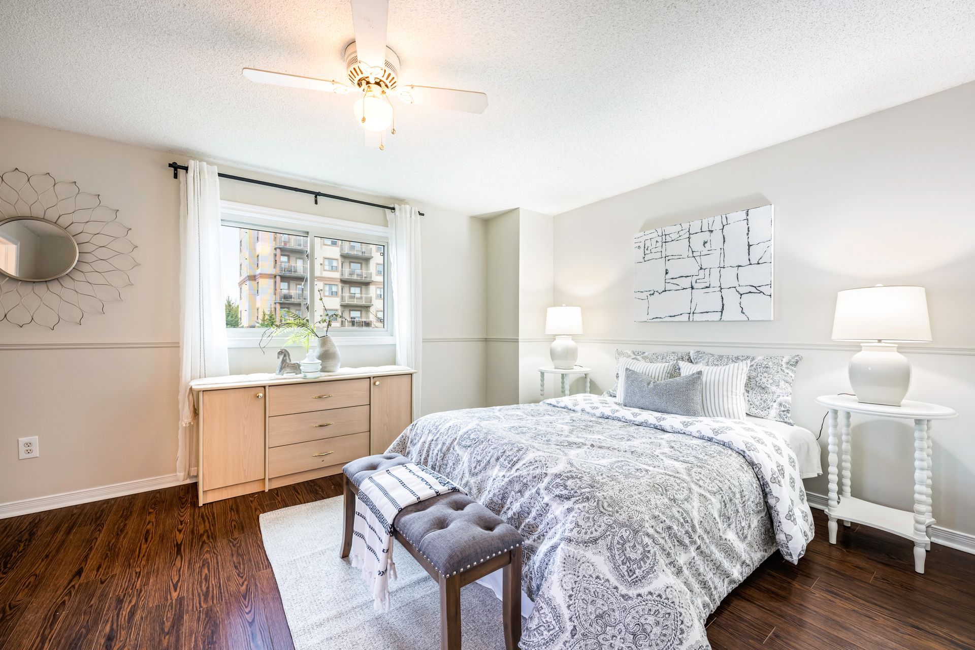 A bedroom with a large bed , a bench , lamps and a window.