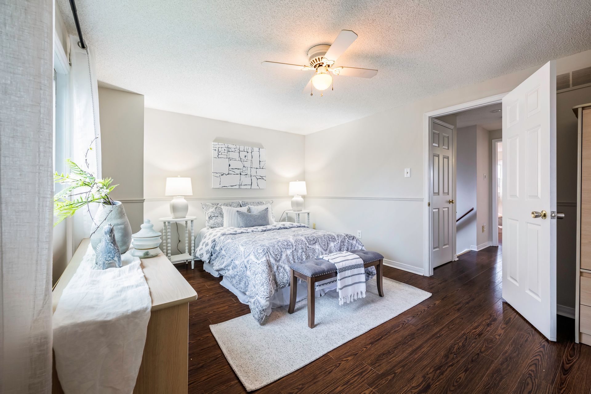 A bedroom with a bed , dresser , bench and ceiling fan.