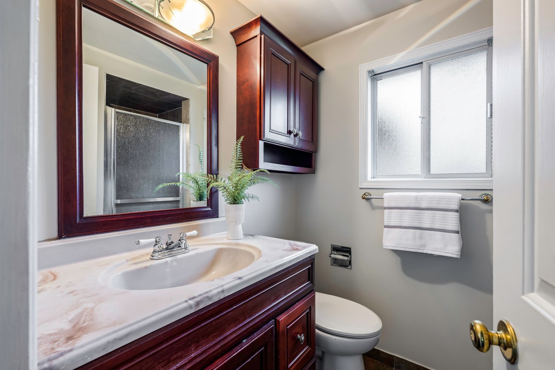 A bathroom with a sink , toilet , mirror and window.