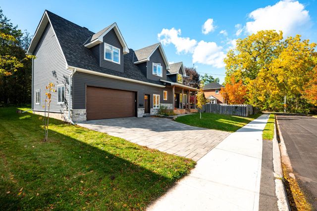 Modern gray house with brown garage, stone driveway, and yellow autumn tree by the sidewalk