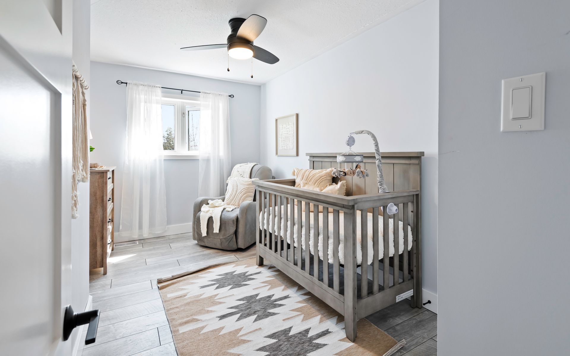 A nursery with a crib , chair , and ceiling fan.