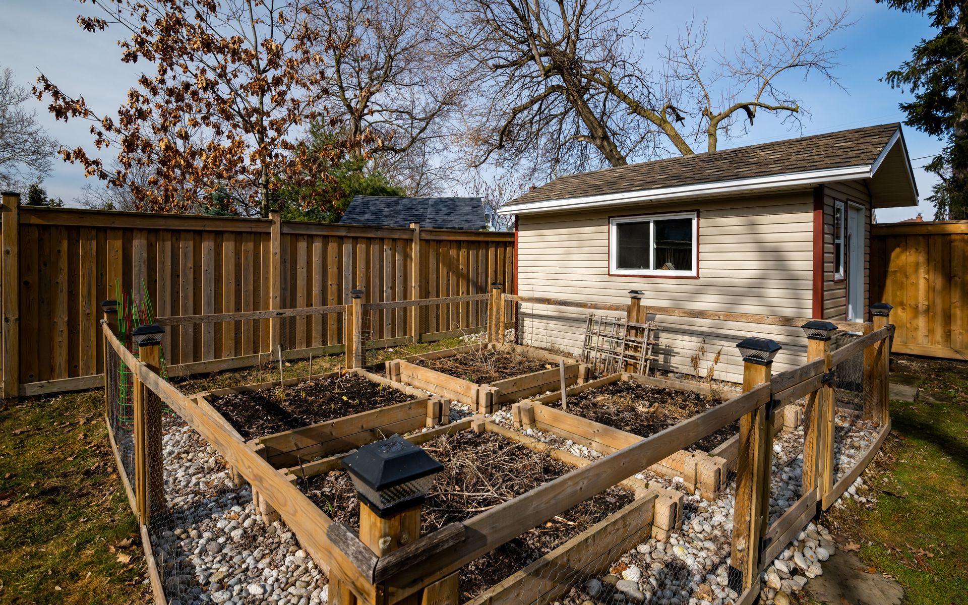 A garden with a wooden fence and a shed in the background.