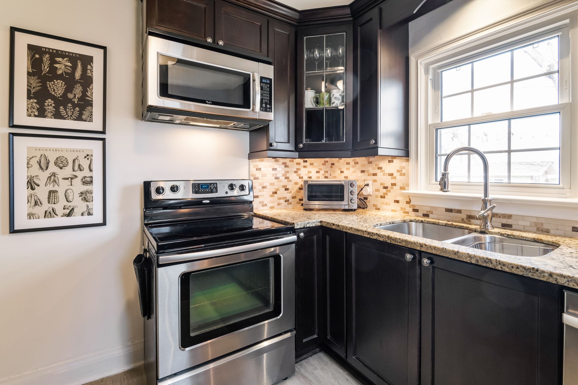 A kitchen with a stove , microwave , sink and window.