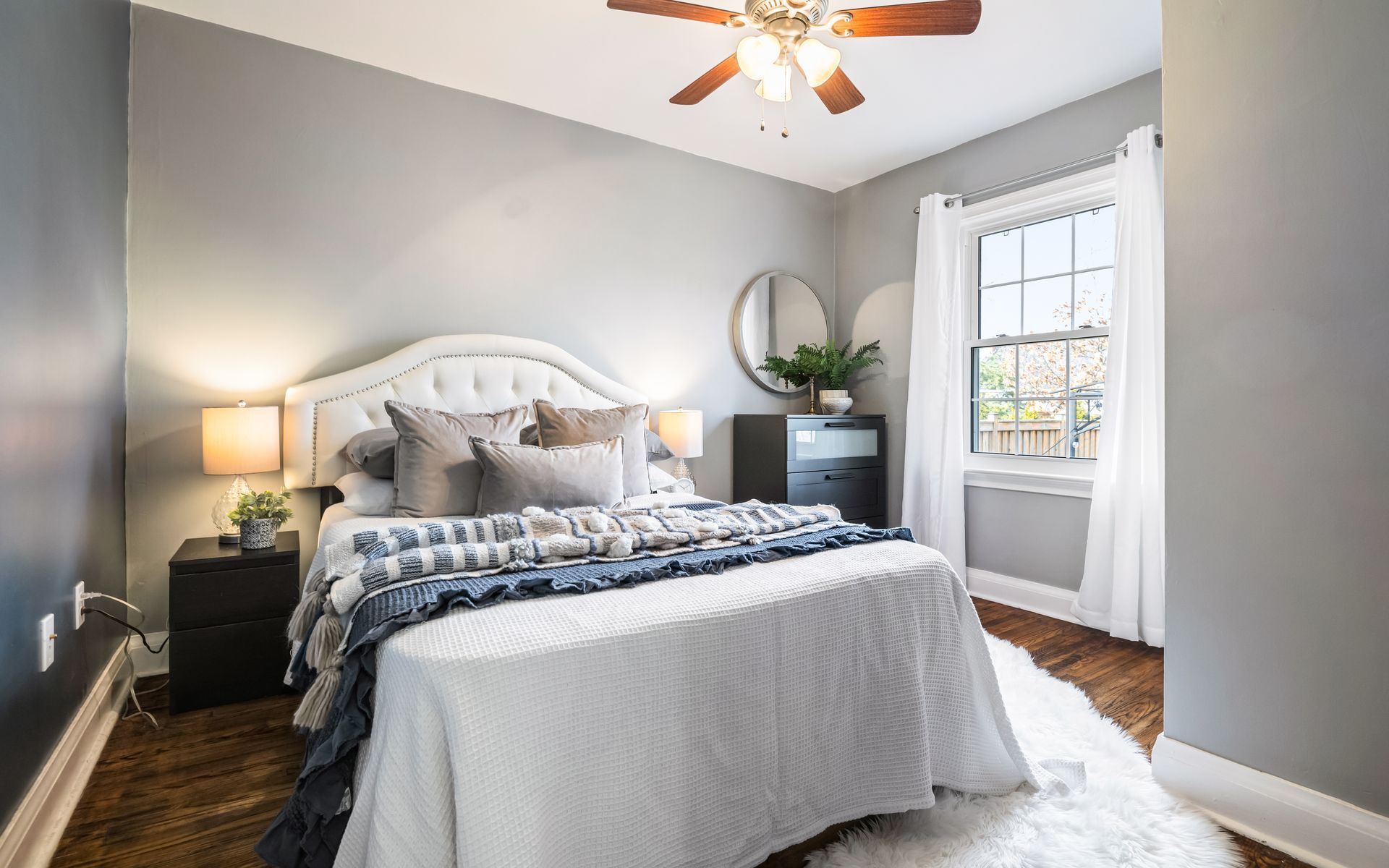 A bedroom with a bed , nightstand , mirror and ceiling fan.