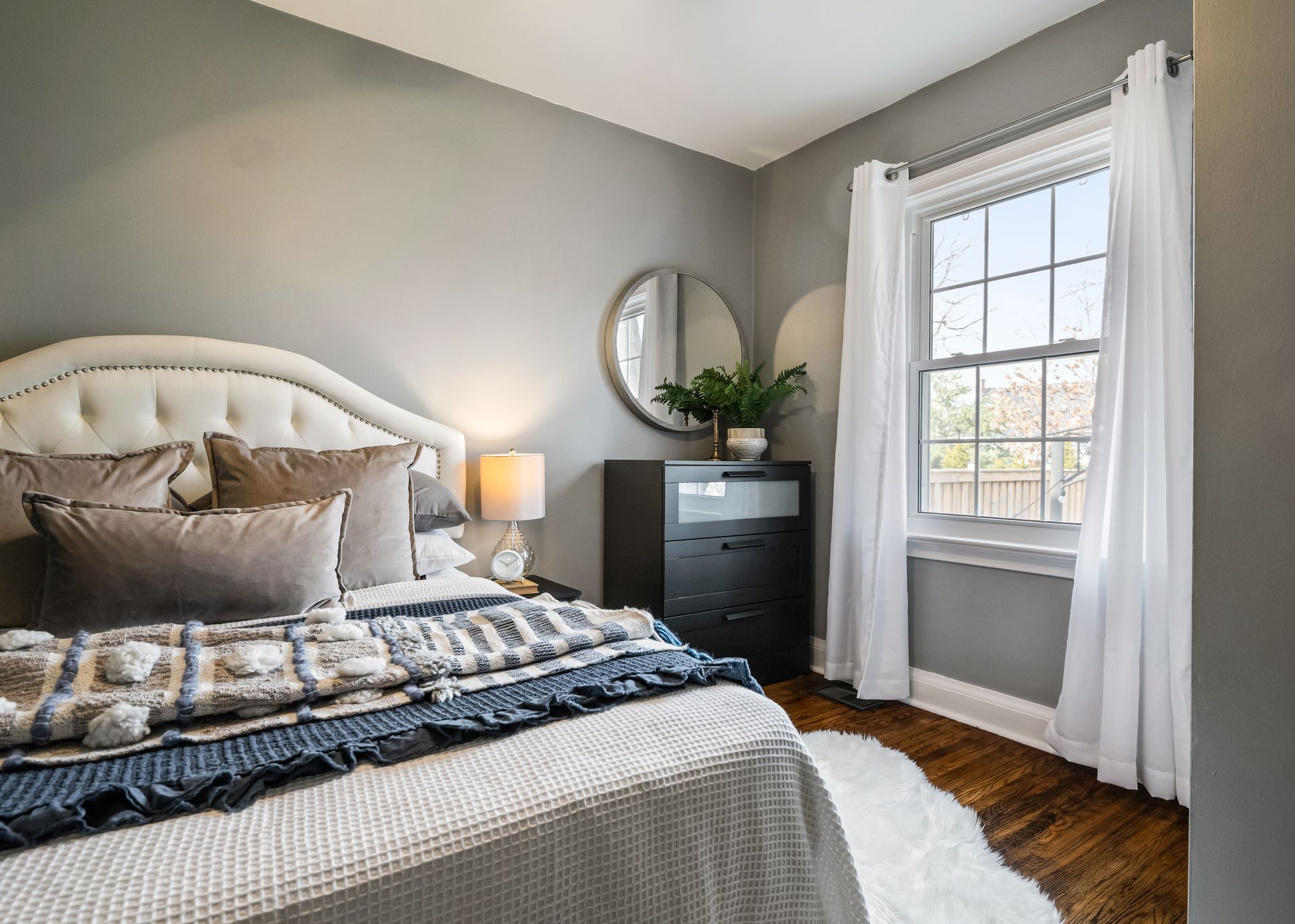 A bedroom with a bed , dresser , mirror and window.