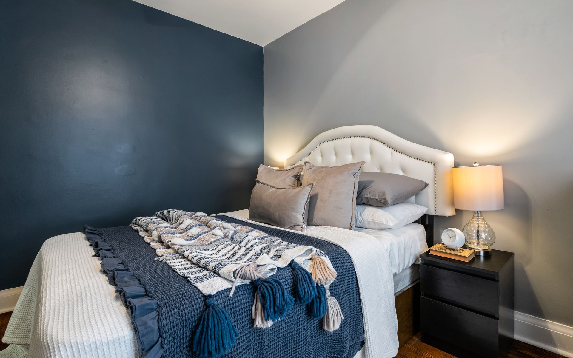 A bedroom with a bed , nightstand , lamp and blue walls.
