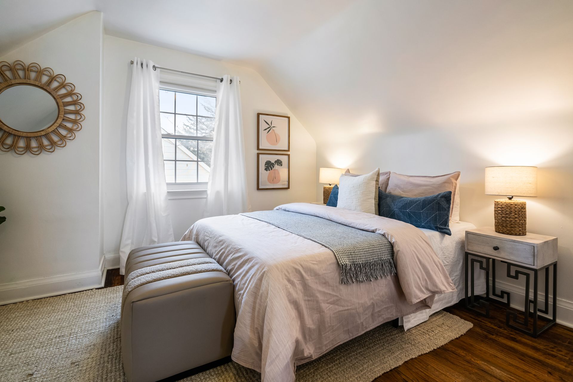 A bedroom with a bed , ottoman , nightstand and mirror.