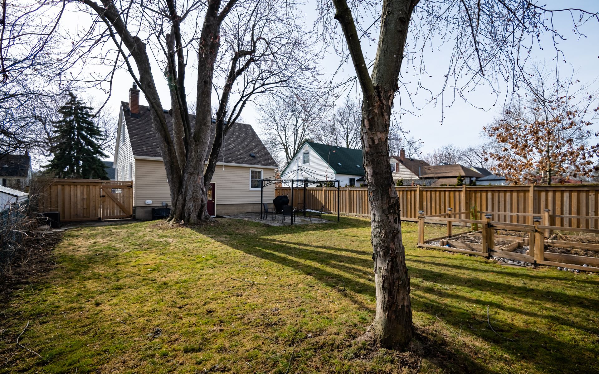 A backyard with a wooden fence and trees in front of a house.