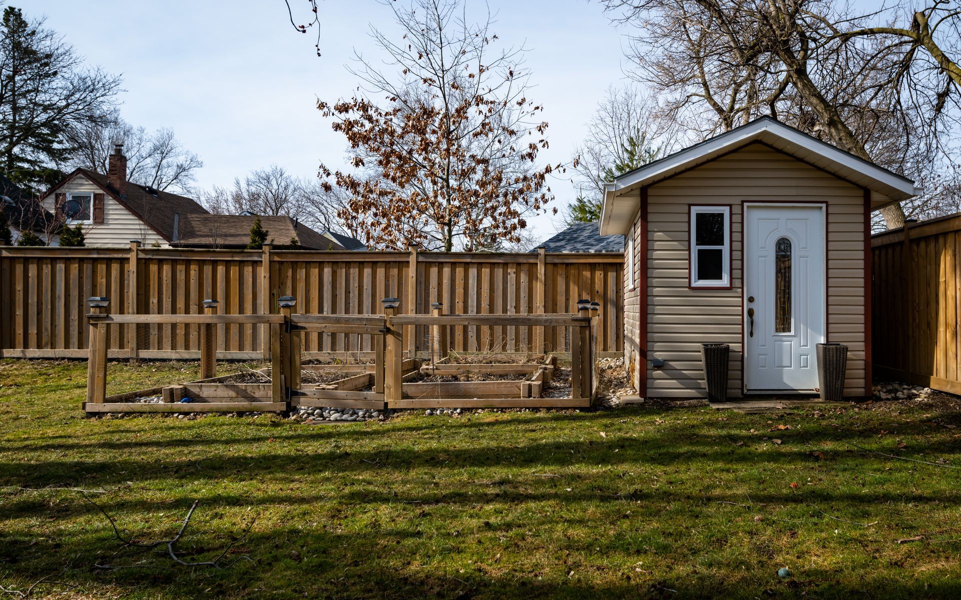 A small shed is sitting in the middle of a lush green yard next to a wooden fence.