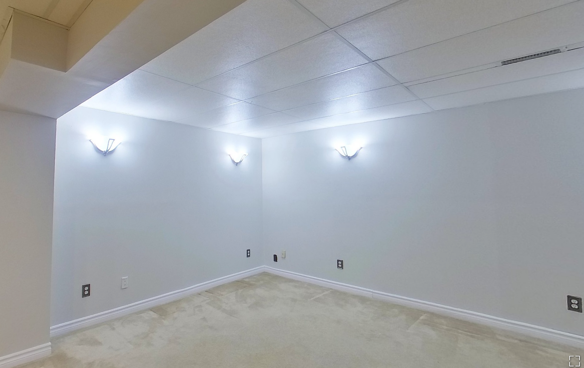 An empty basement with white walls and a carpeted floor.