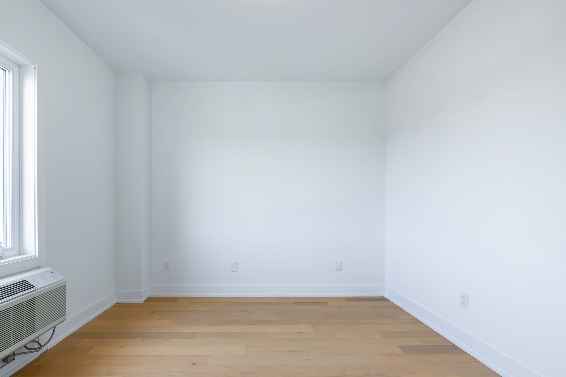 An empty room with hardwood floors , white walls and a window.