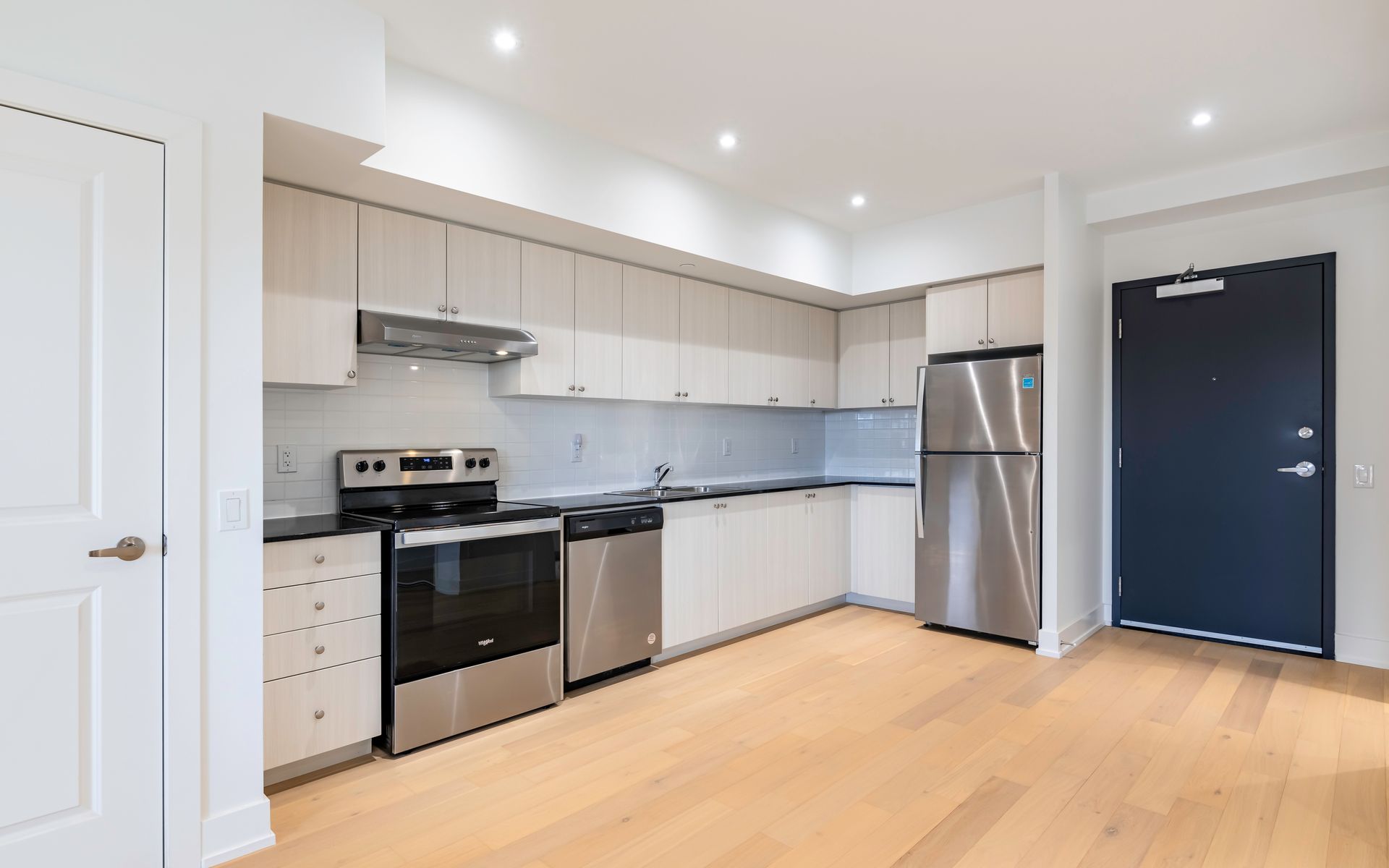 An empty kitchen with stainless steel appliances and white cabinets