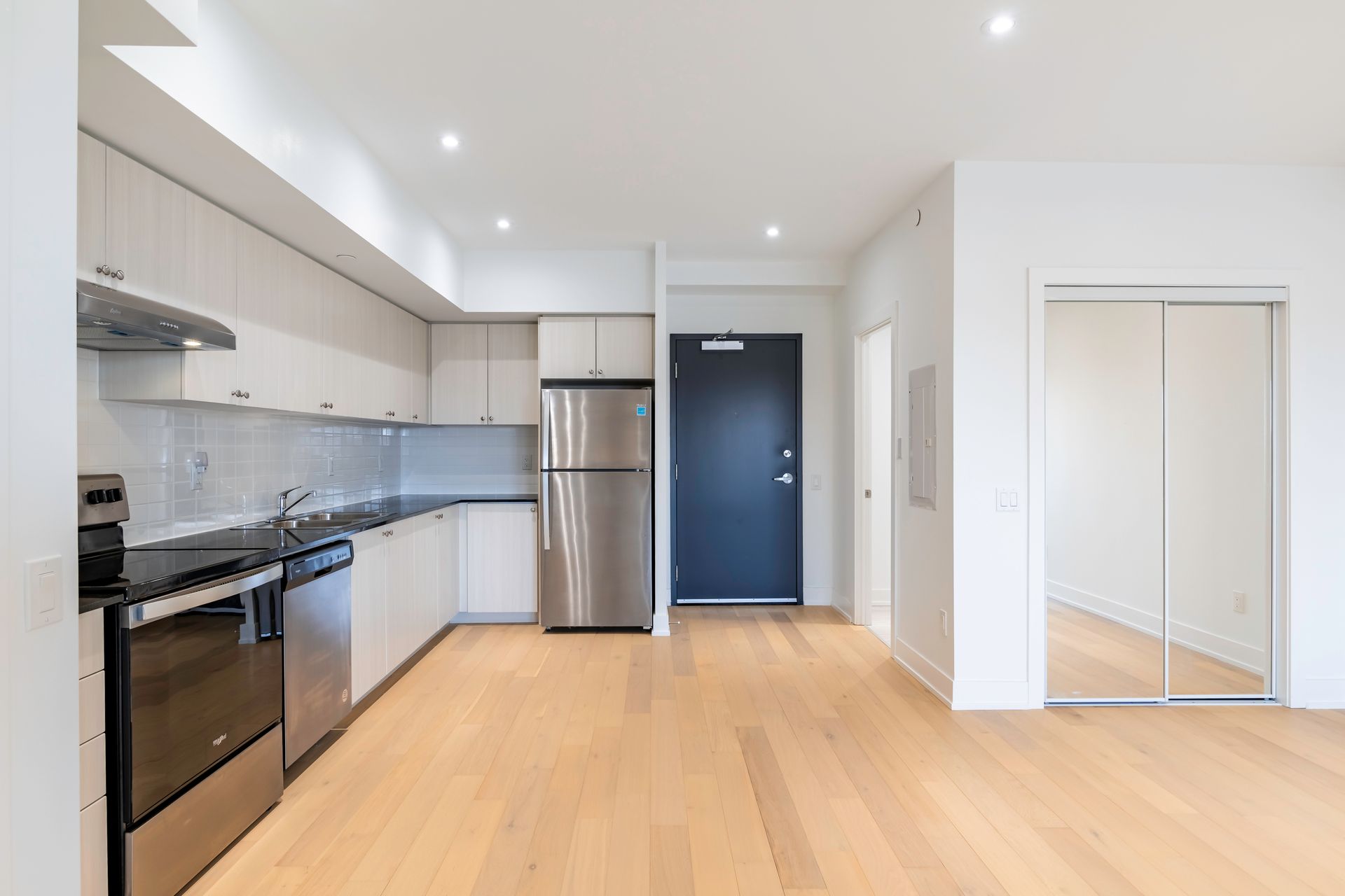 A kitchen with stainless steel appliances and hardwood floors in an empty apartment.