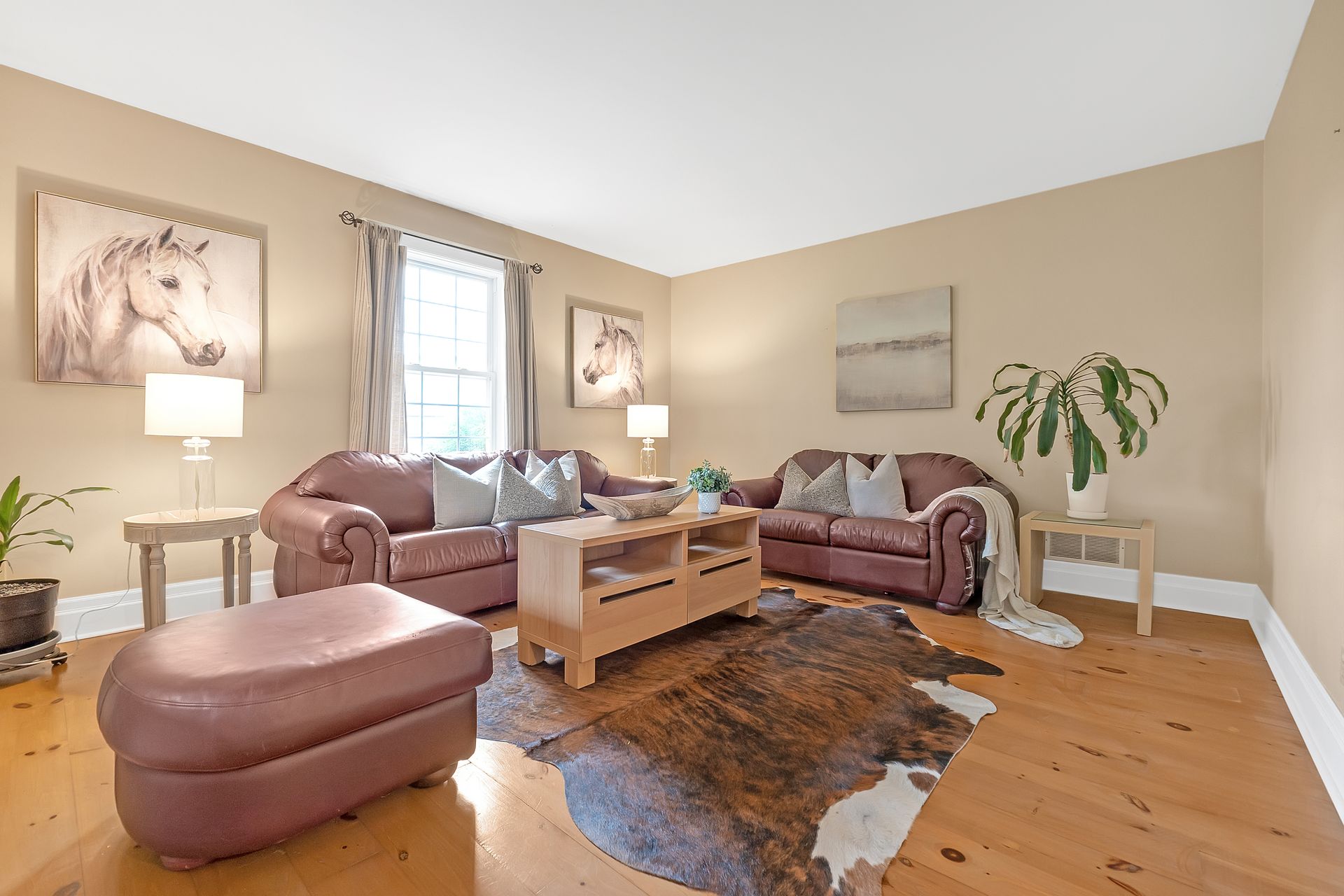 A living room with two couches , an ottoman , a coffee table and a cowhide rug.