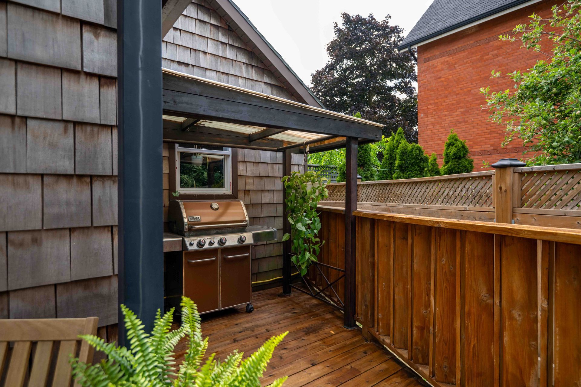A wooden deck with a grill under a pergola.