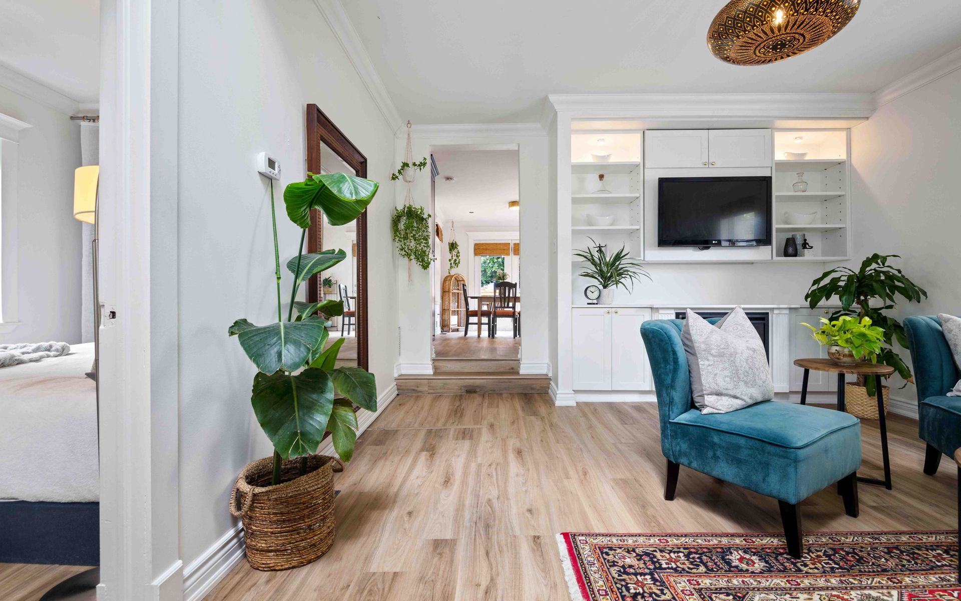 A living room with hardwood floors , two chairs , a plant and a television.