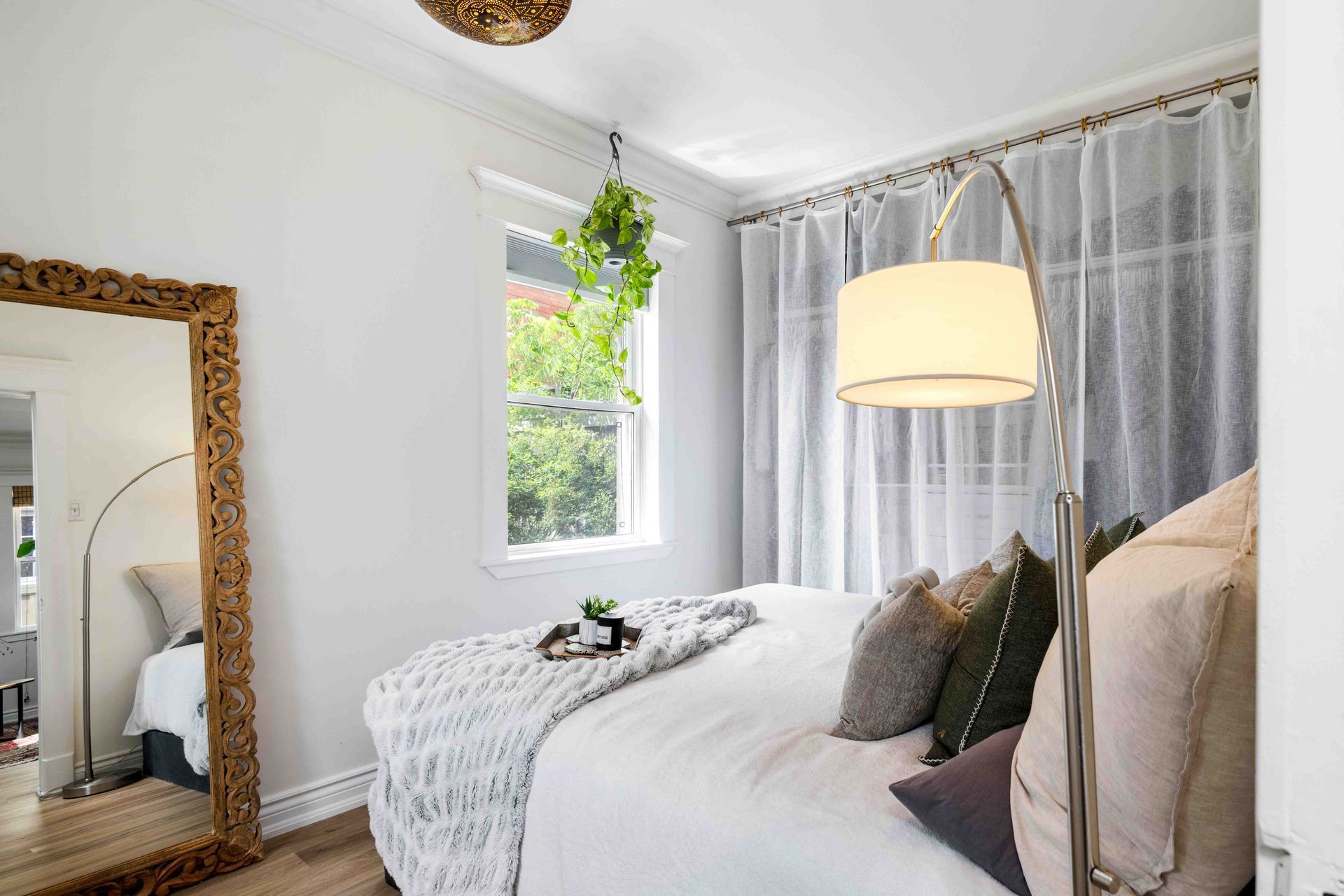 A bedroom with a bed , lamp , mirror and window.