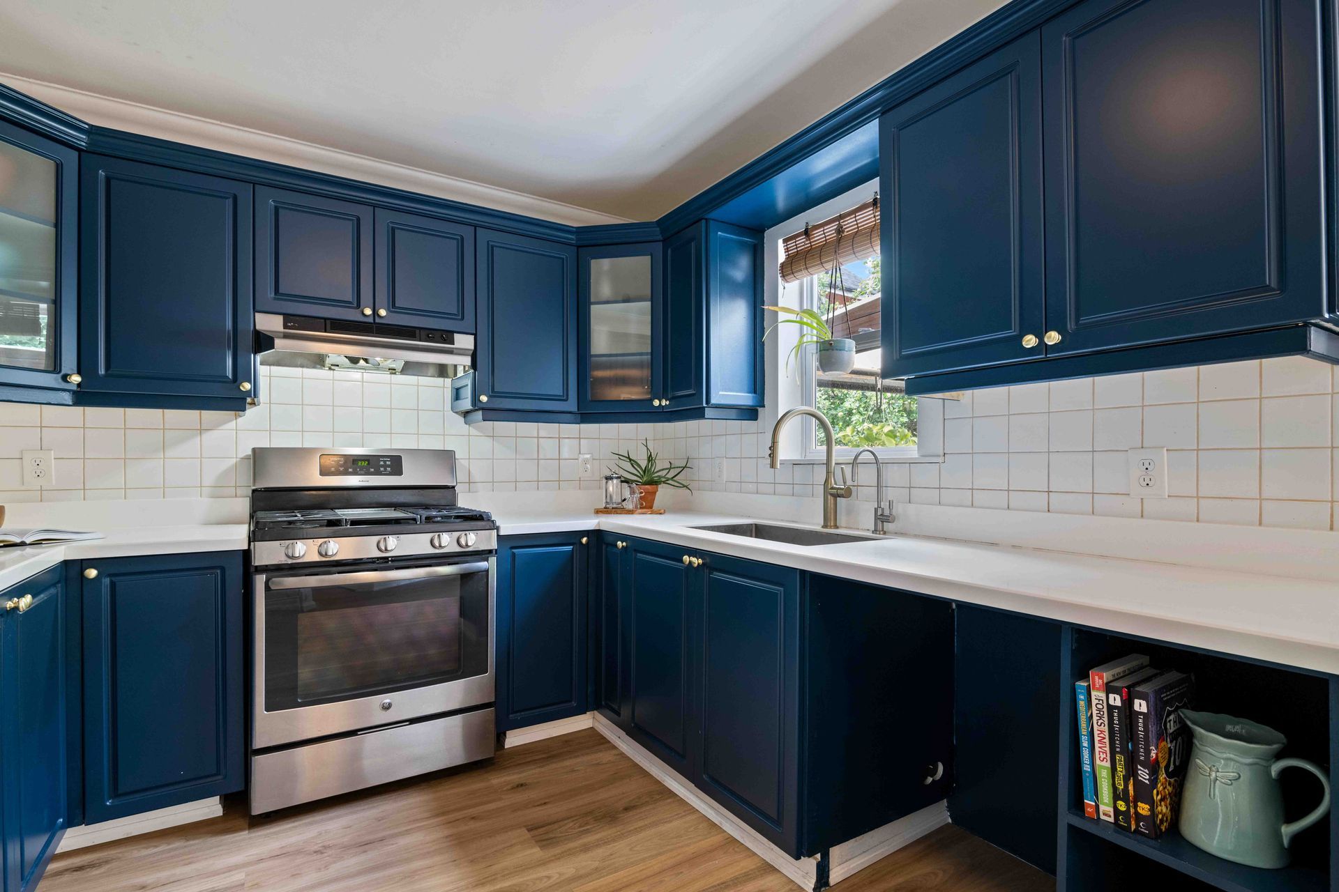 A kitchen with blue cabinets , a stove , a sink , and a window.