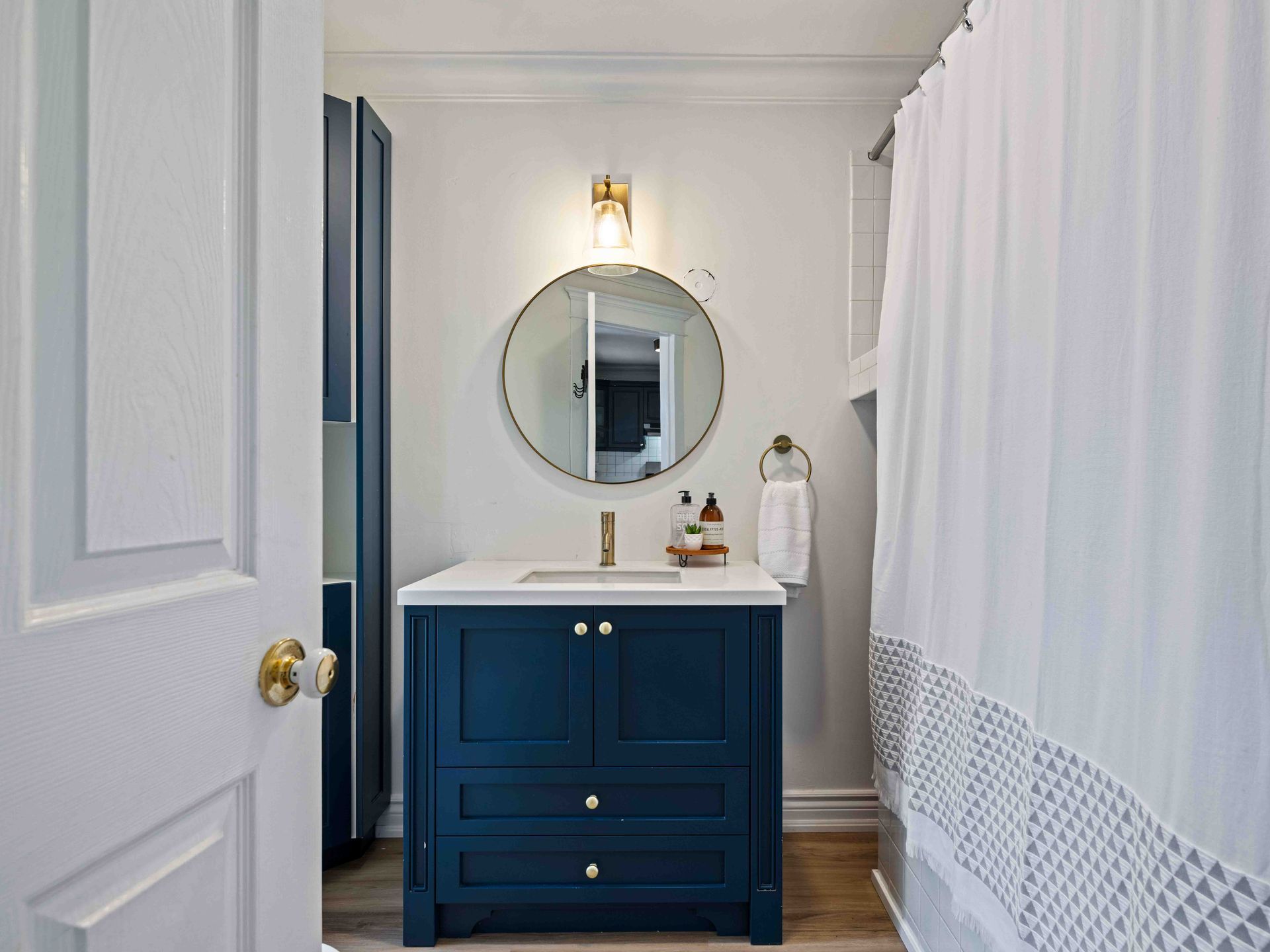 A bathroom with a blue vanity , a round mirror , and a shower curtain.