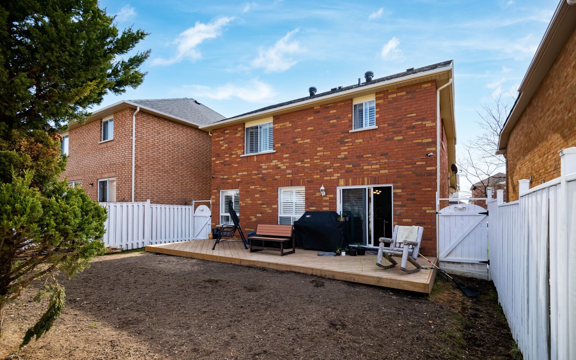 The backyard of a brick house with a wooden deck and a white fence.