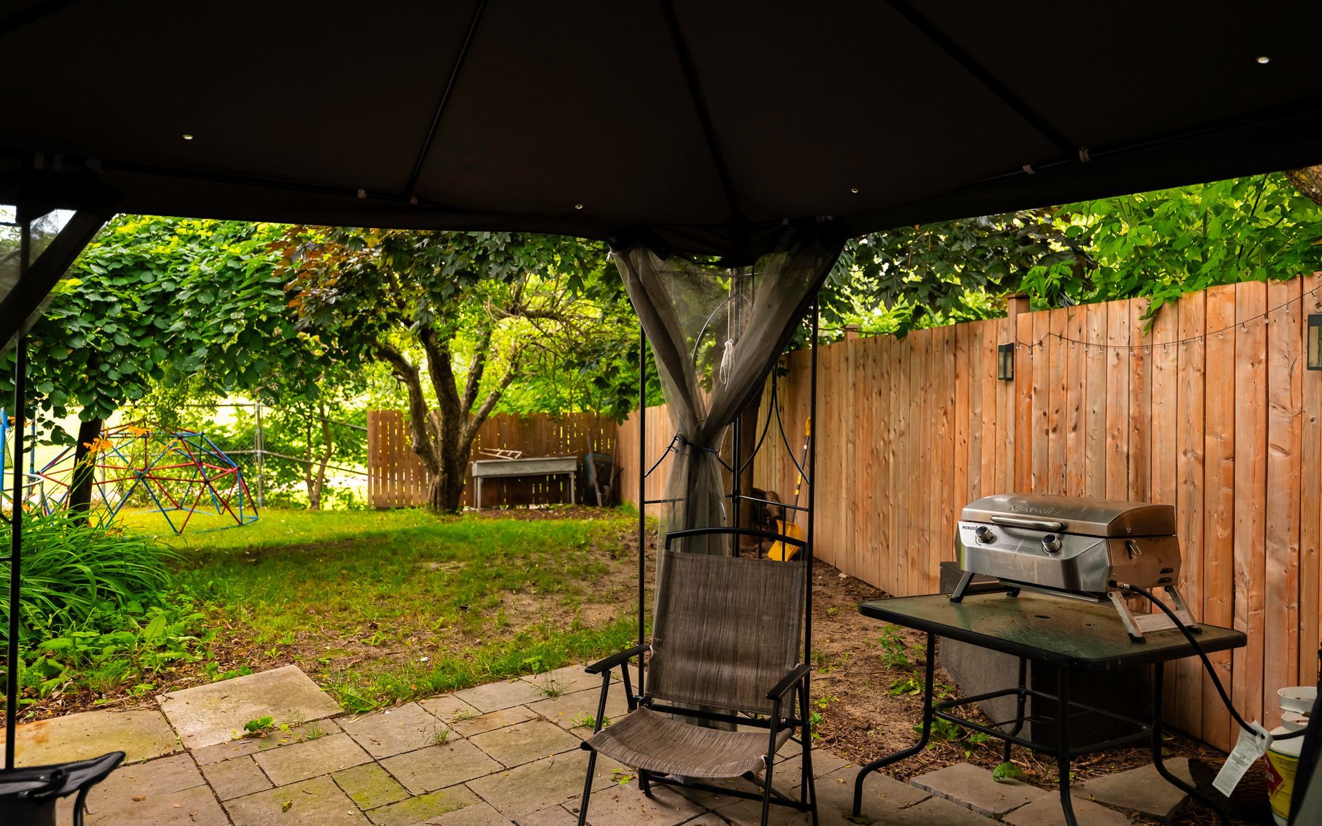 There is a gazebo in the backyard with a table and chairs underneath it.