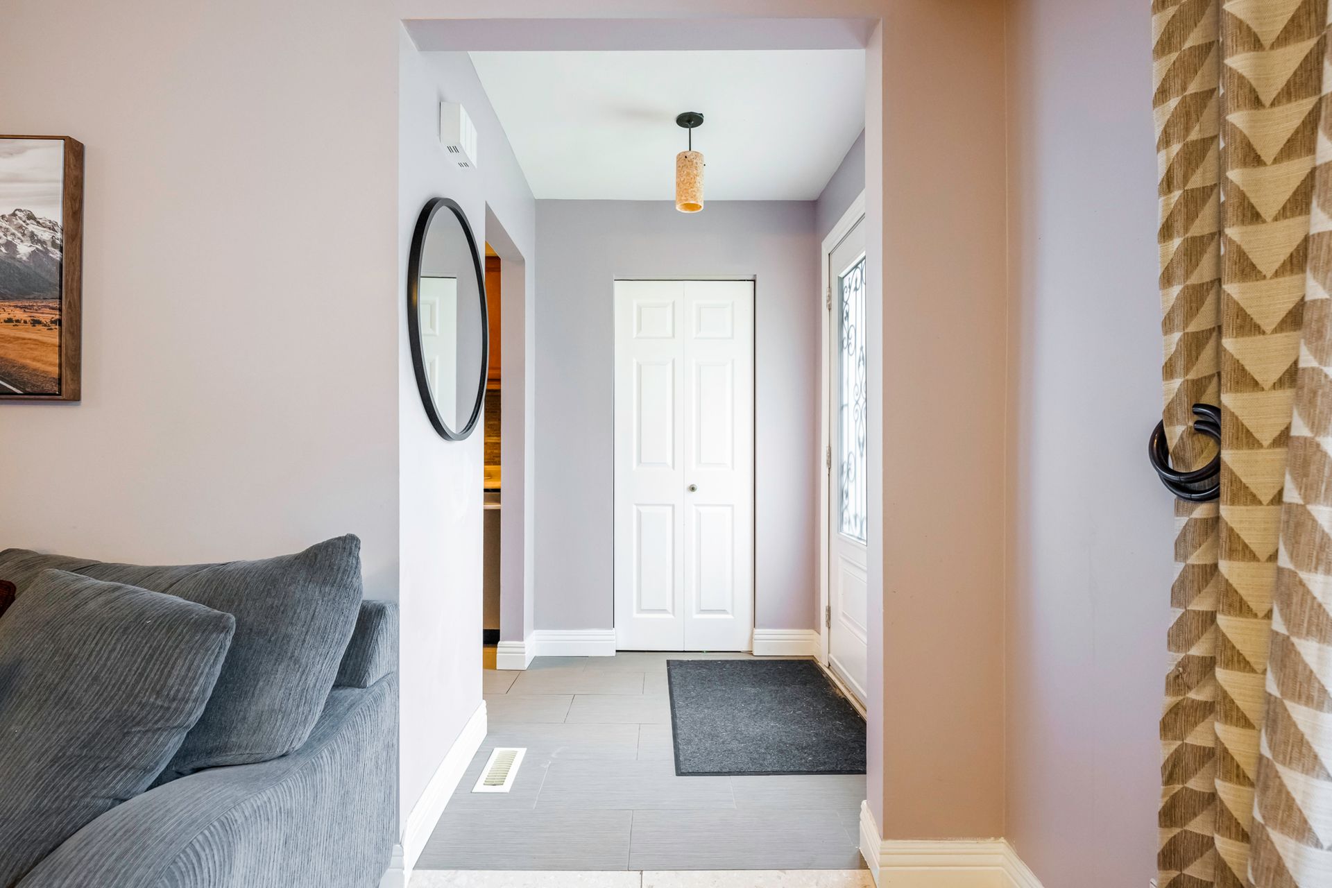 A living room with a couch and a mirror looking into a hallway.