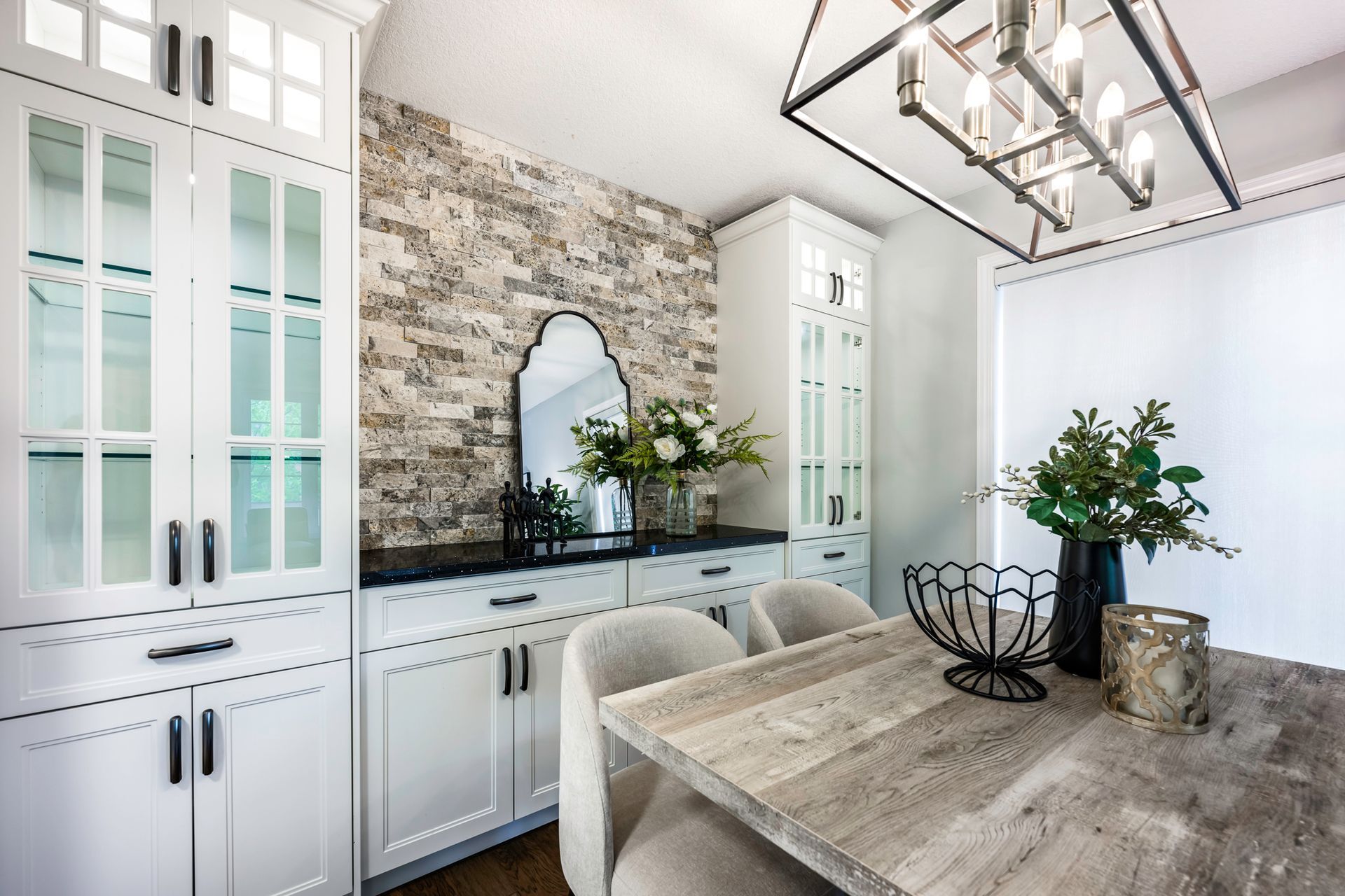 A dining room with a wooden table , chairs , cabinets and a mirror.