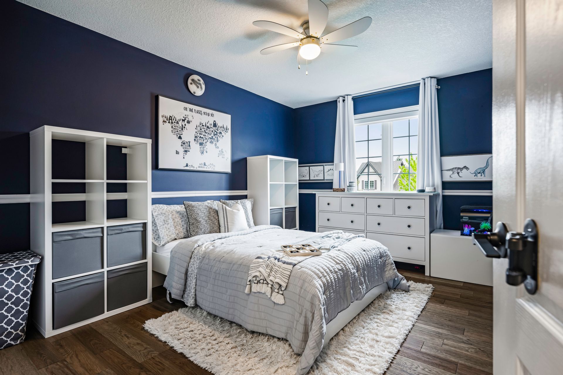 A bedroom with a bed , dresser , shelves and a ceiling fan.