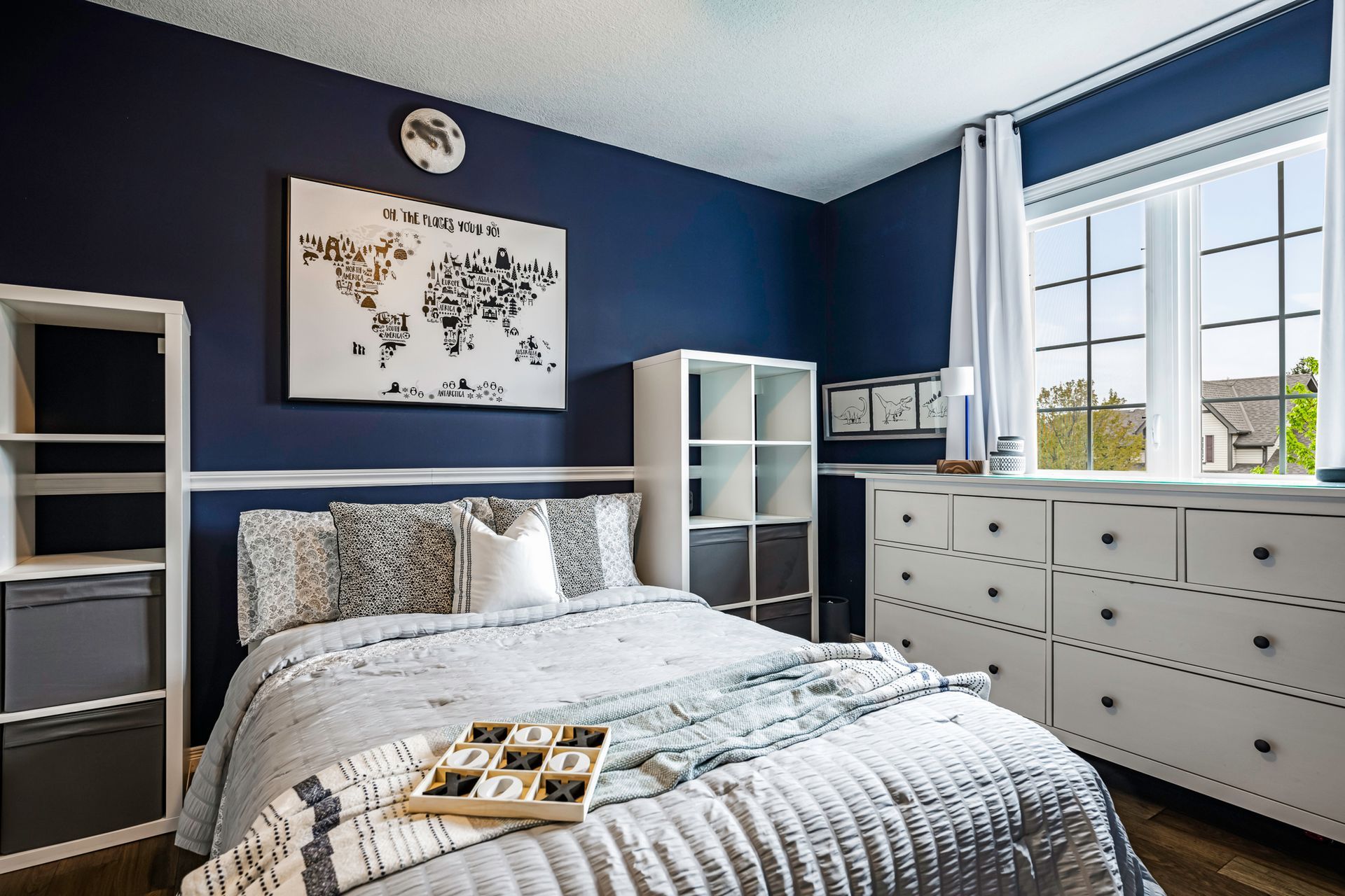 A bedroom with a bed , dresser , shelves and a map on the wall.