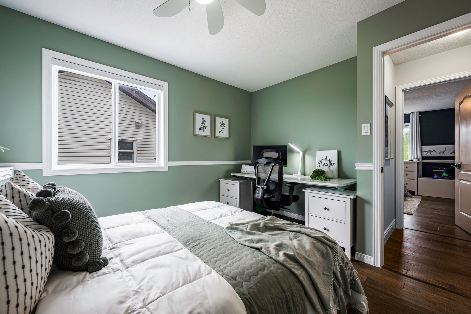 A bedroom with green walls , a bed , a desk and a ceiling fan.