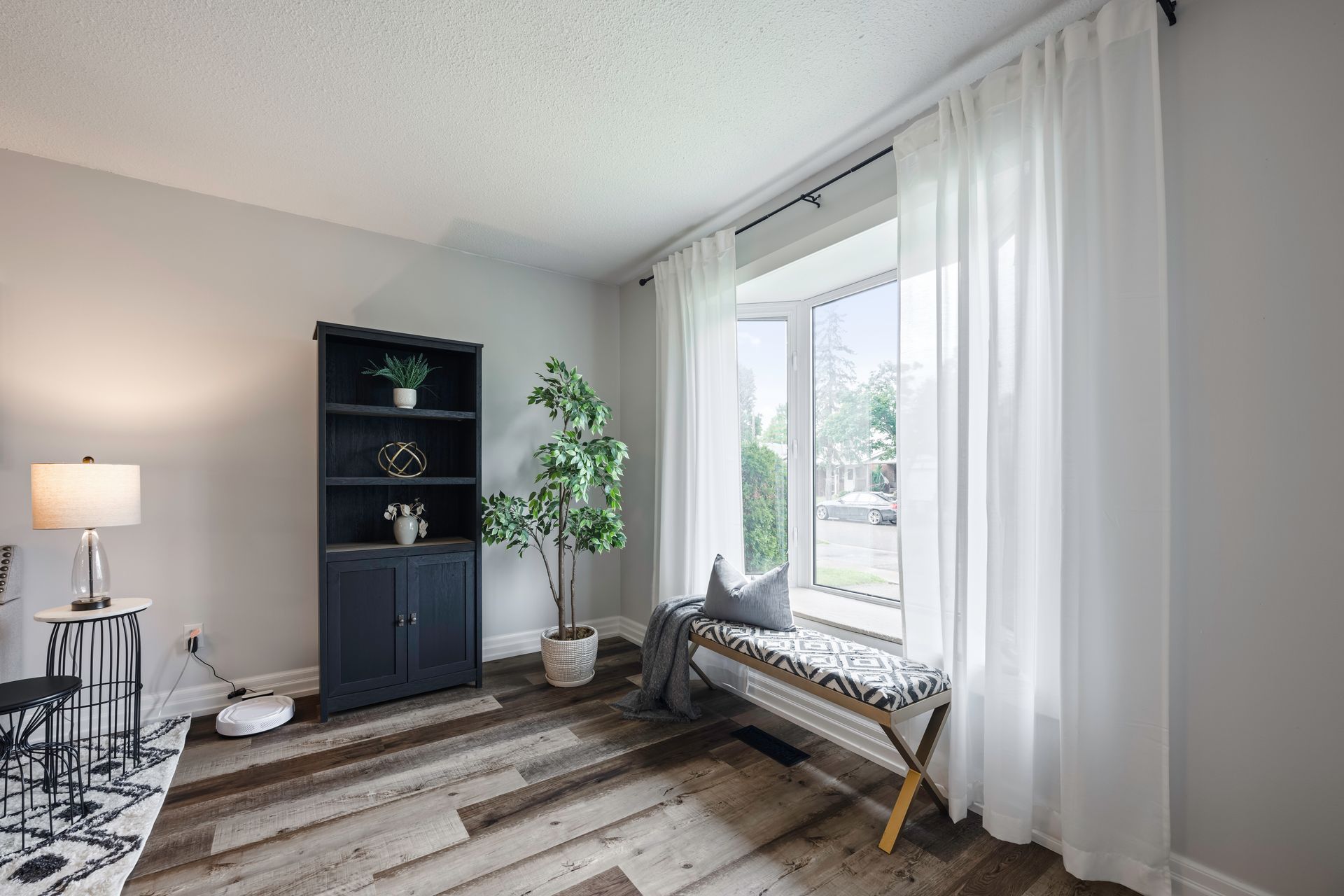 A living room with hardwood floors , a bookshelf , a bench and a window.