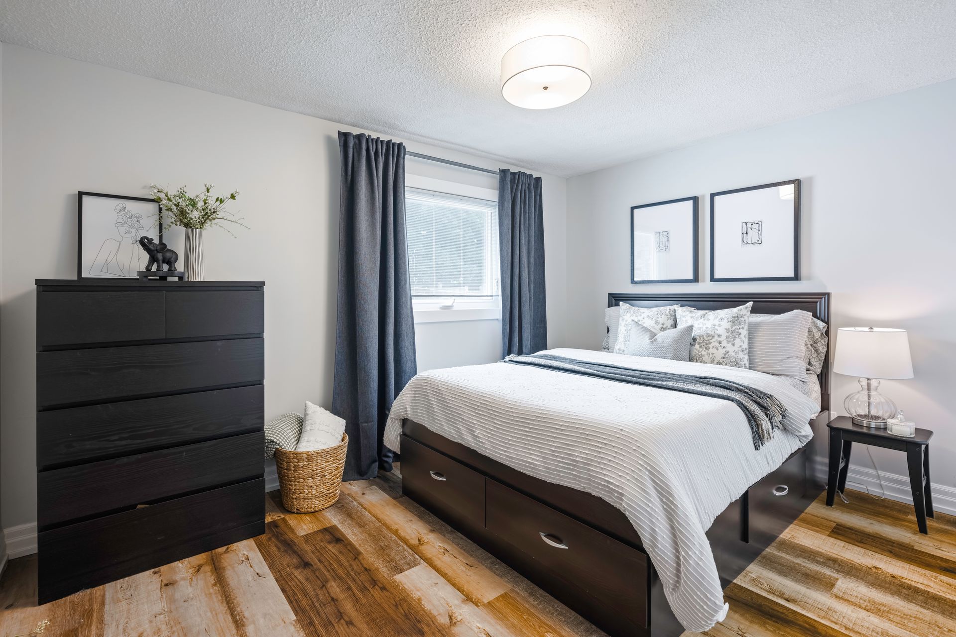 A bedroom with a bed , dresser , nightstand and window.