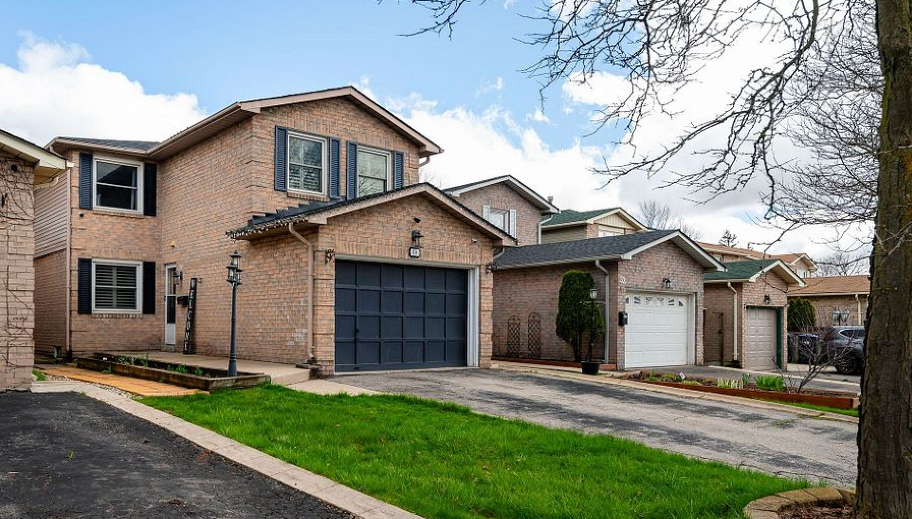 A large brick house with two garages and a large lawn in front of it.
