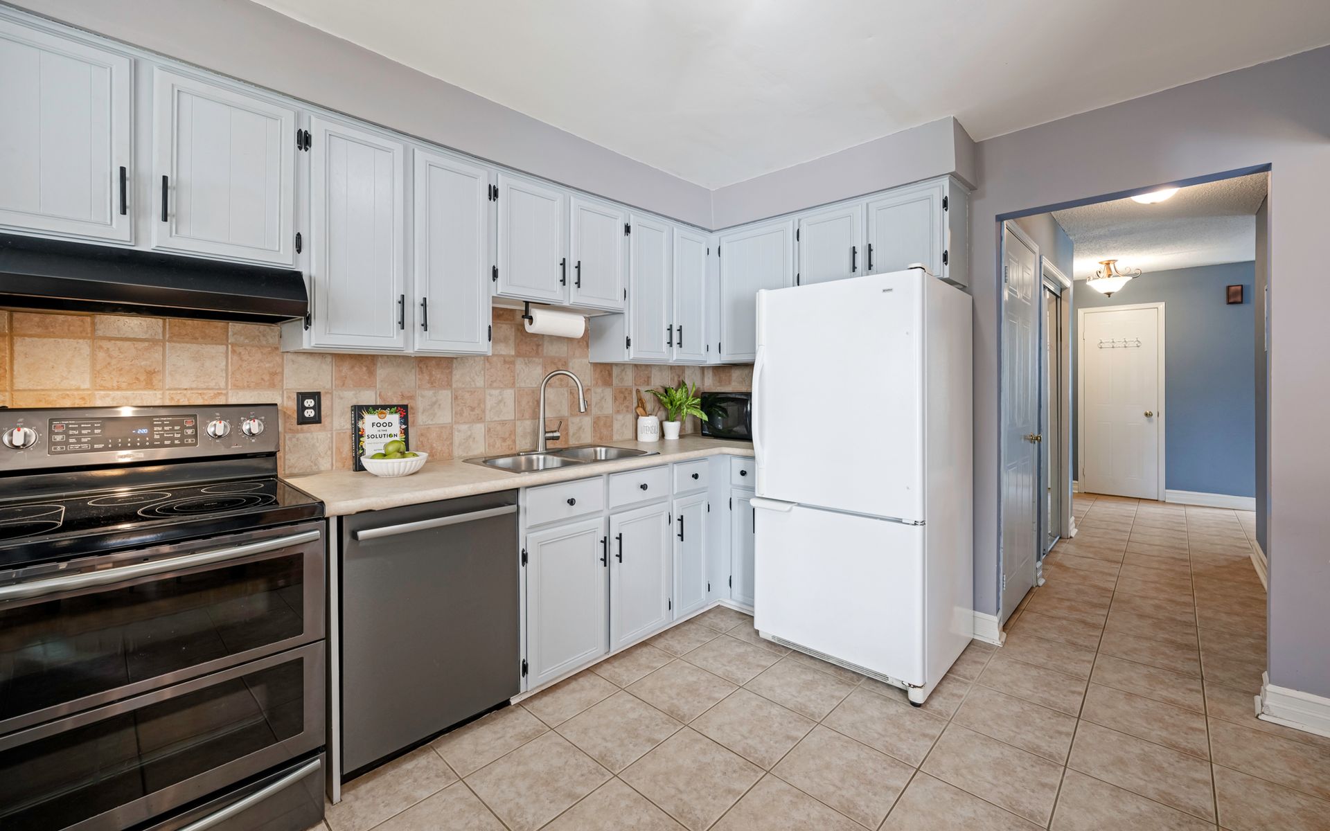 A kitchen with white cabinets , a stove , a refrigerator , and a dishwasher.