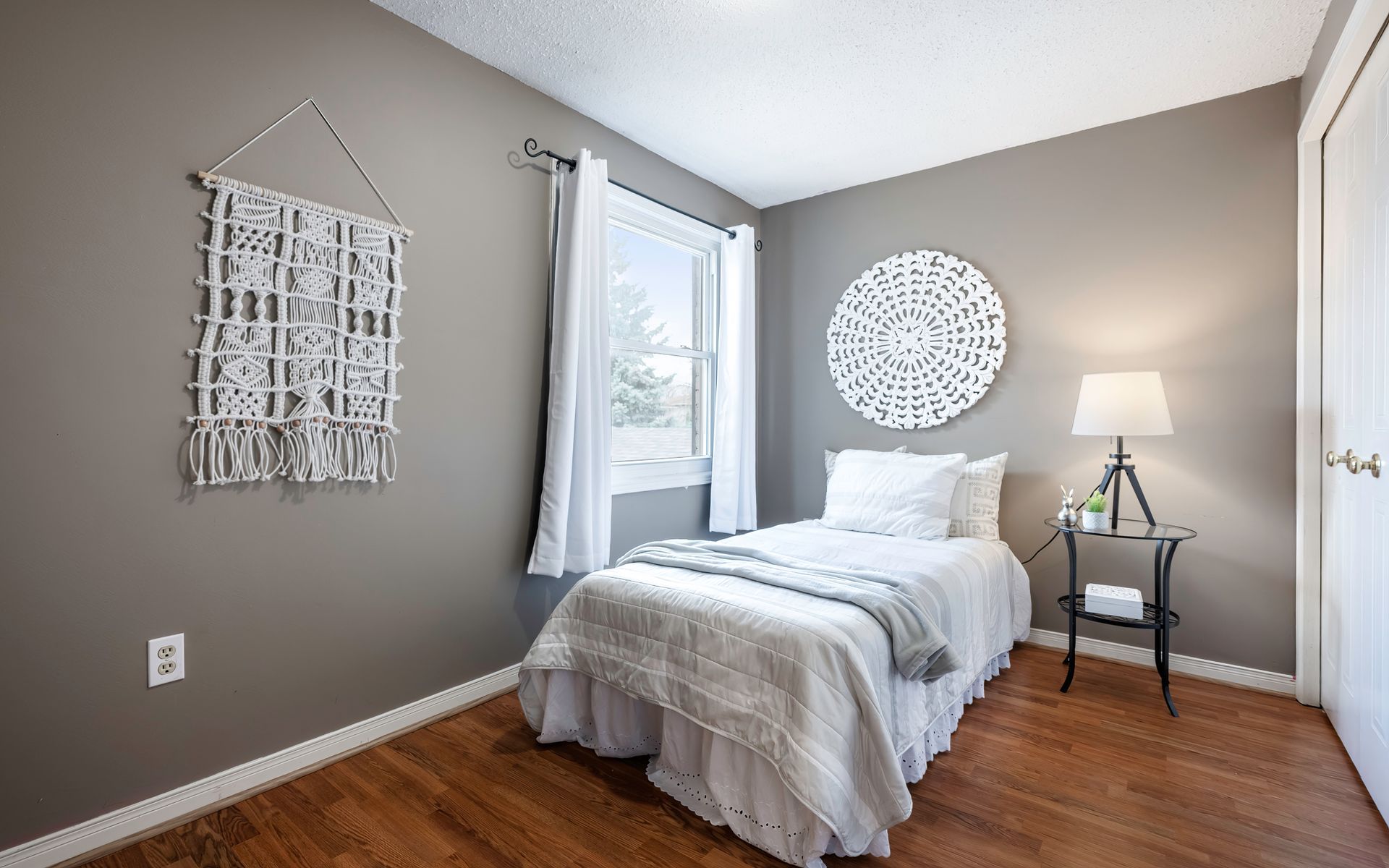A bedroom with a bed , nightstand , lamp and window.