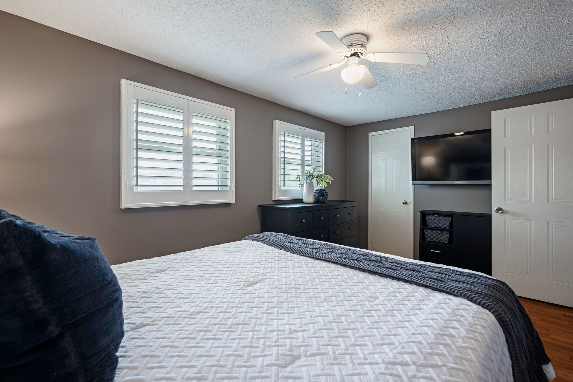 A bedroom with a bed , ceiling fan , television and shutters.