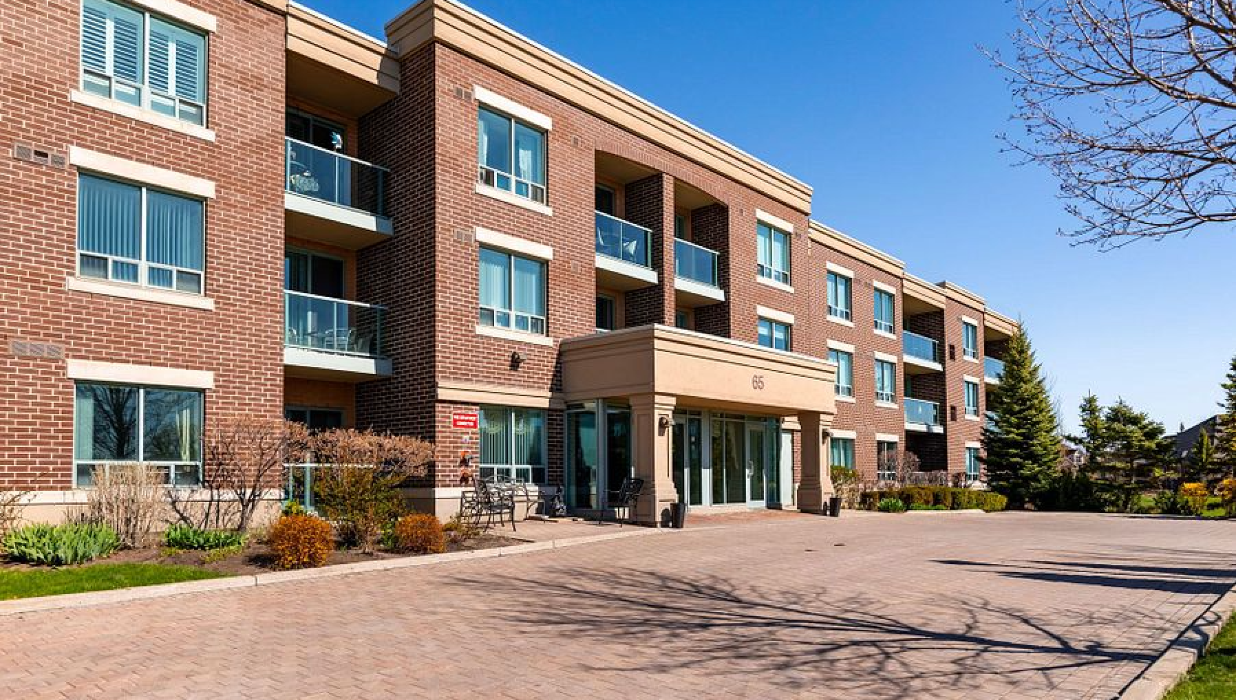 A brick apartment building with balconies and a parking lot in front of it.