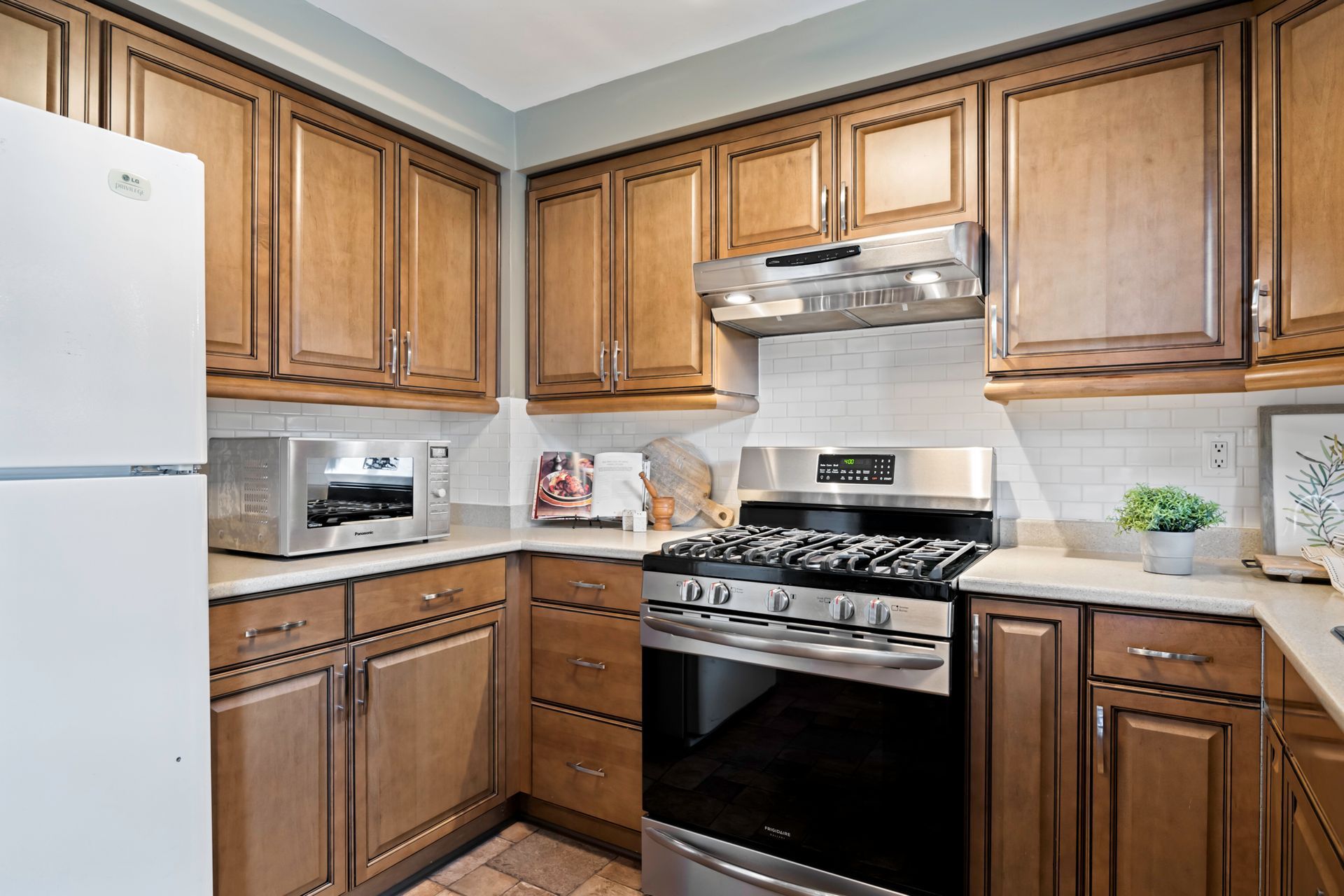 A kitchen with wooden cabinets , stainless steel appliances , a refrigerator , stove and microwave.