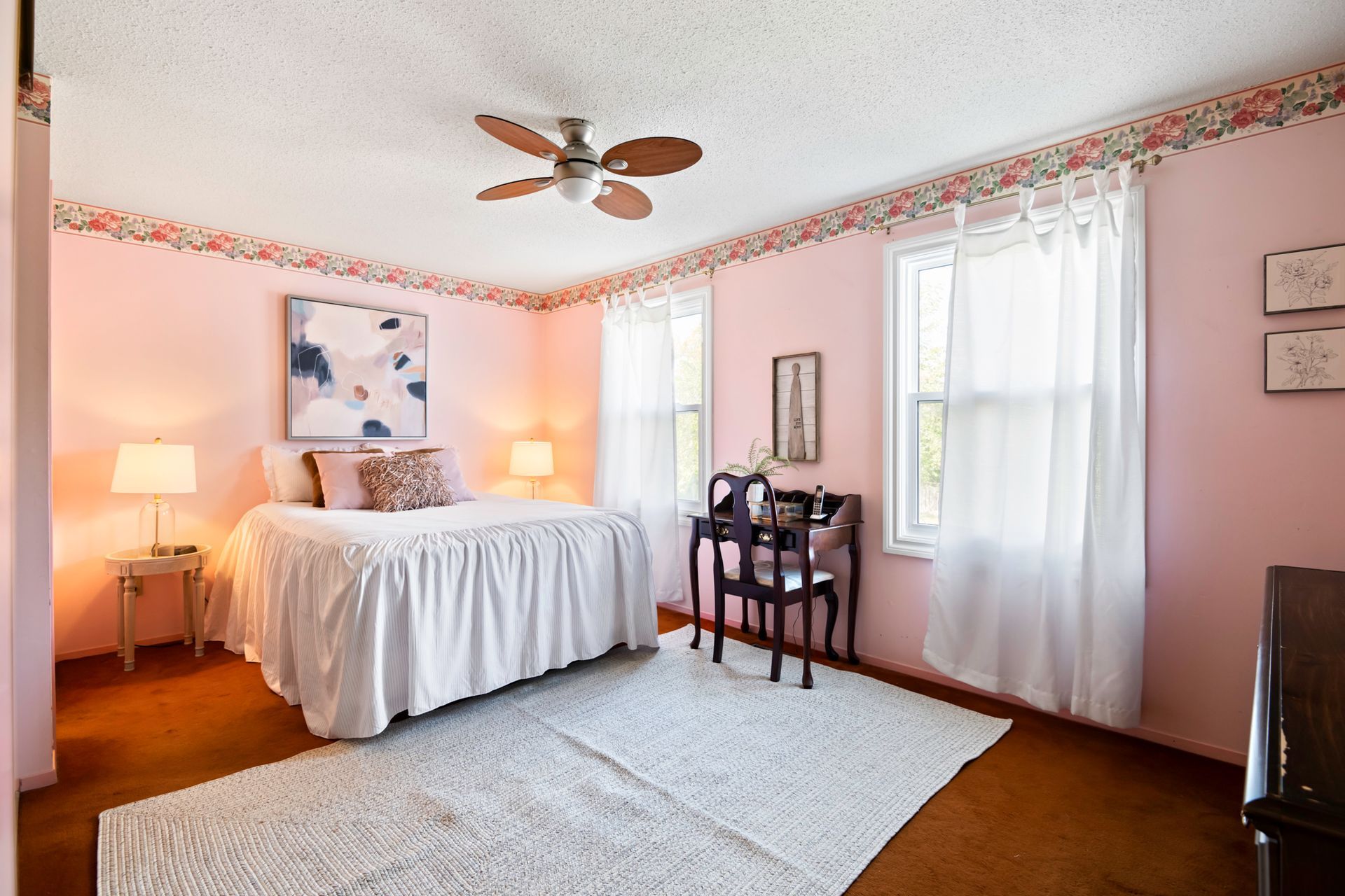 A bedroom with pink walls , a bed , a desk and a ceiling fan.