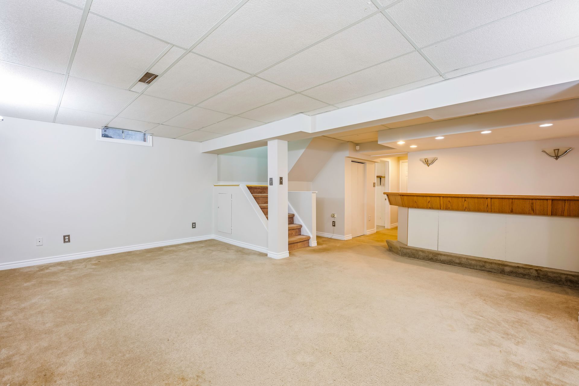 An empty basement with a staircase and a bar.