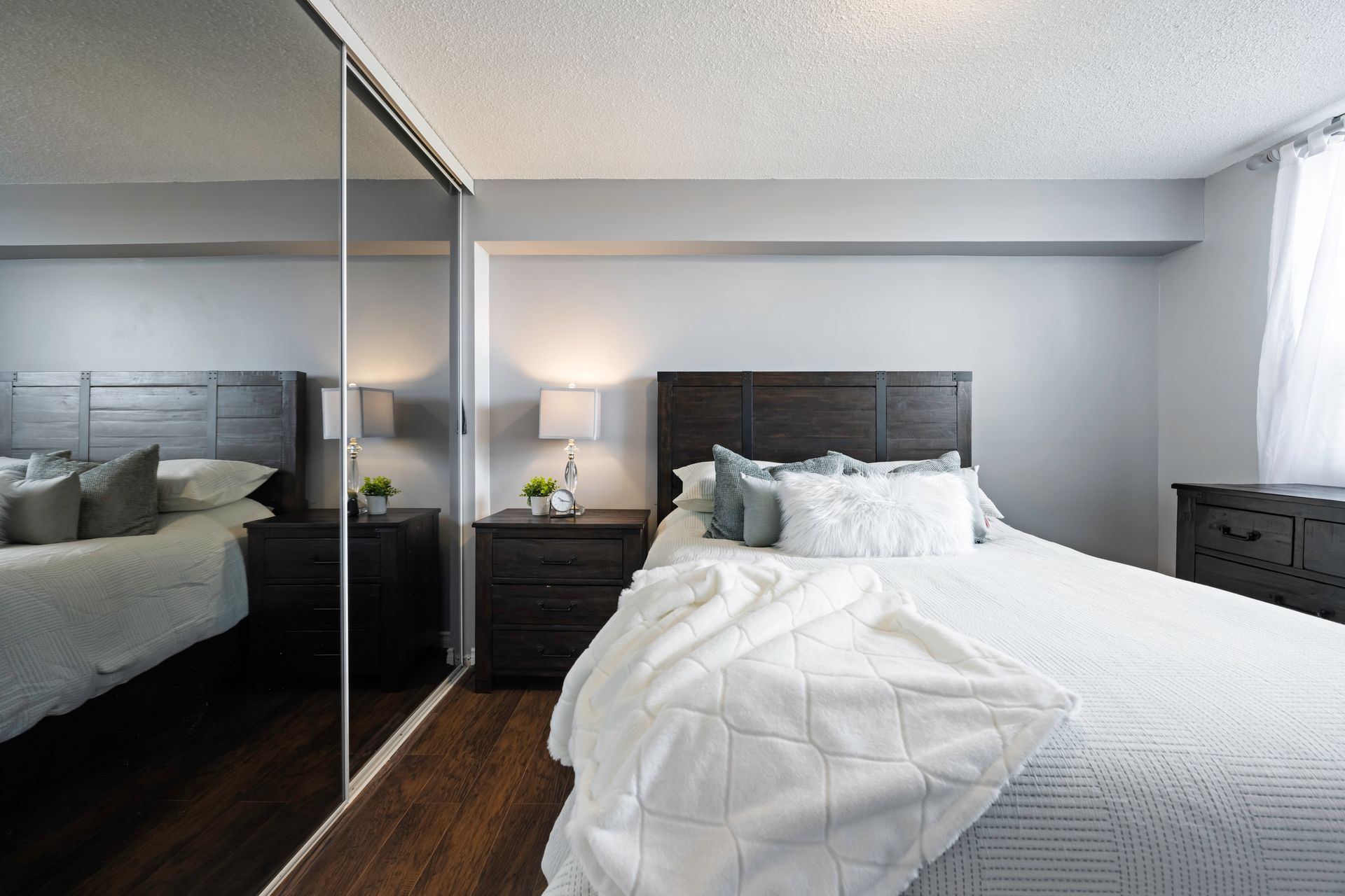A bedroom with a bed , nightstands , dresser and mirrors.