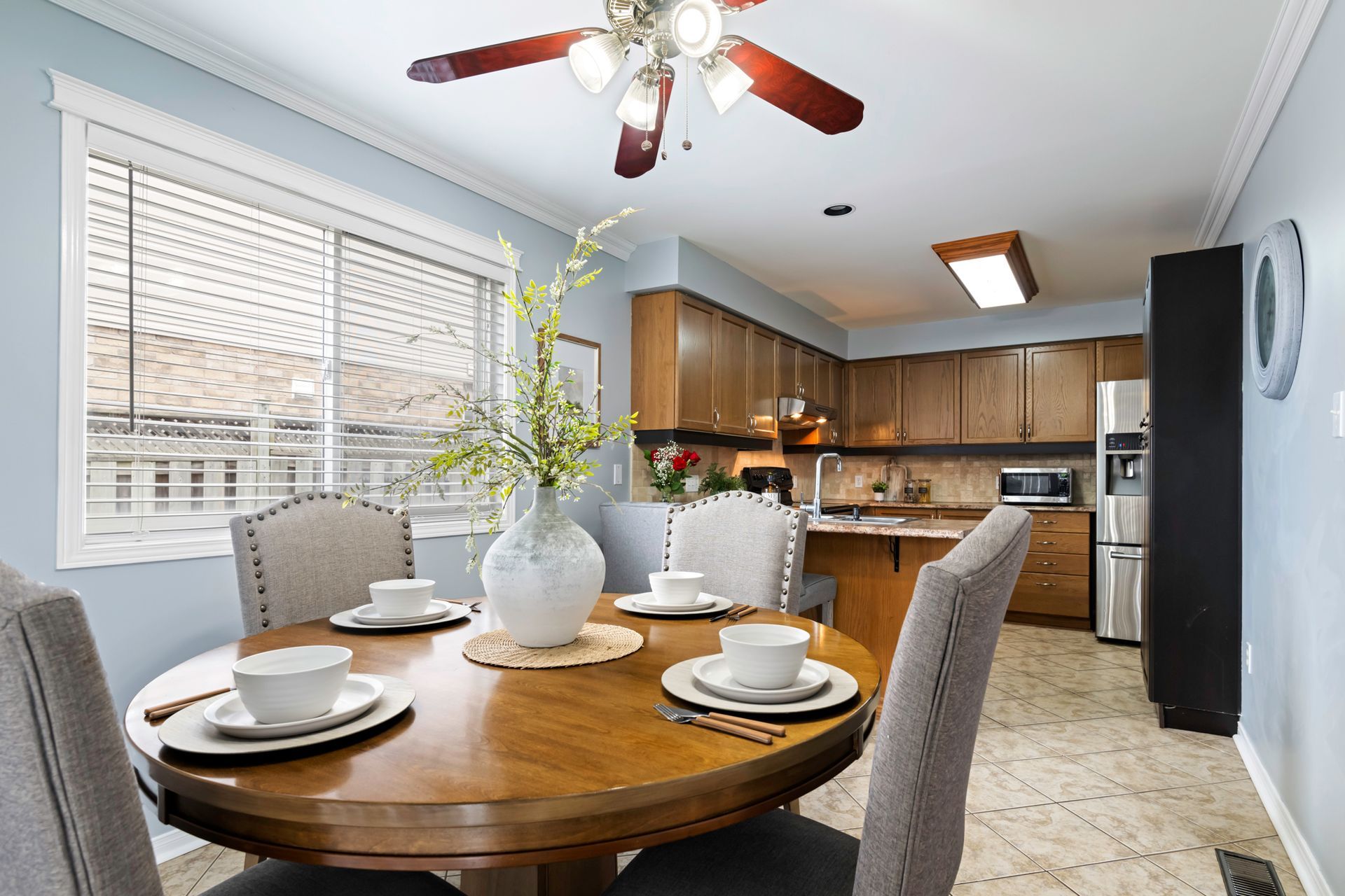 A dining room with a round table and chairs and a ceiling fan.