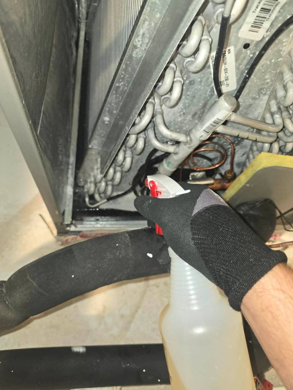 Gloved hand spraying cleaner into a dirty metal appliance interior with a spray bottle