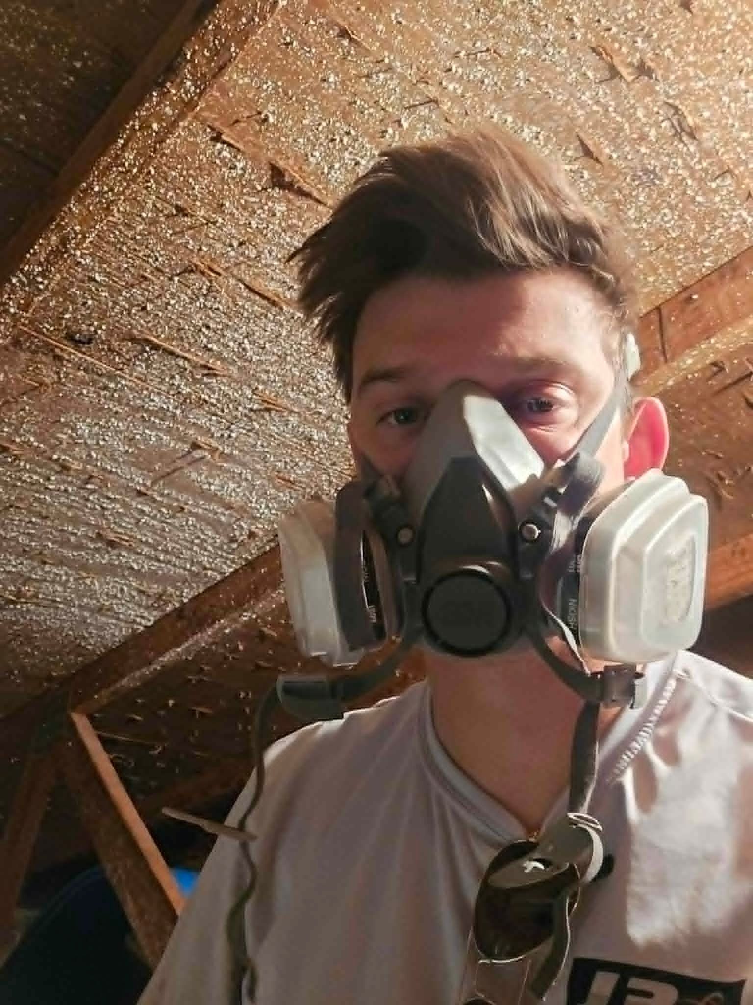 Person wearing a respirator mask indoors under a slanted wooden ceiling.