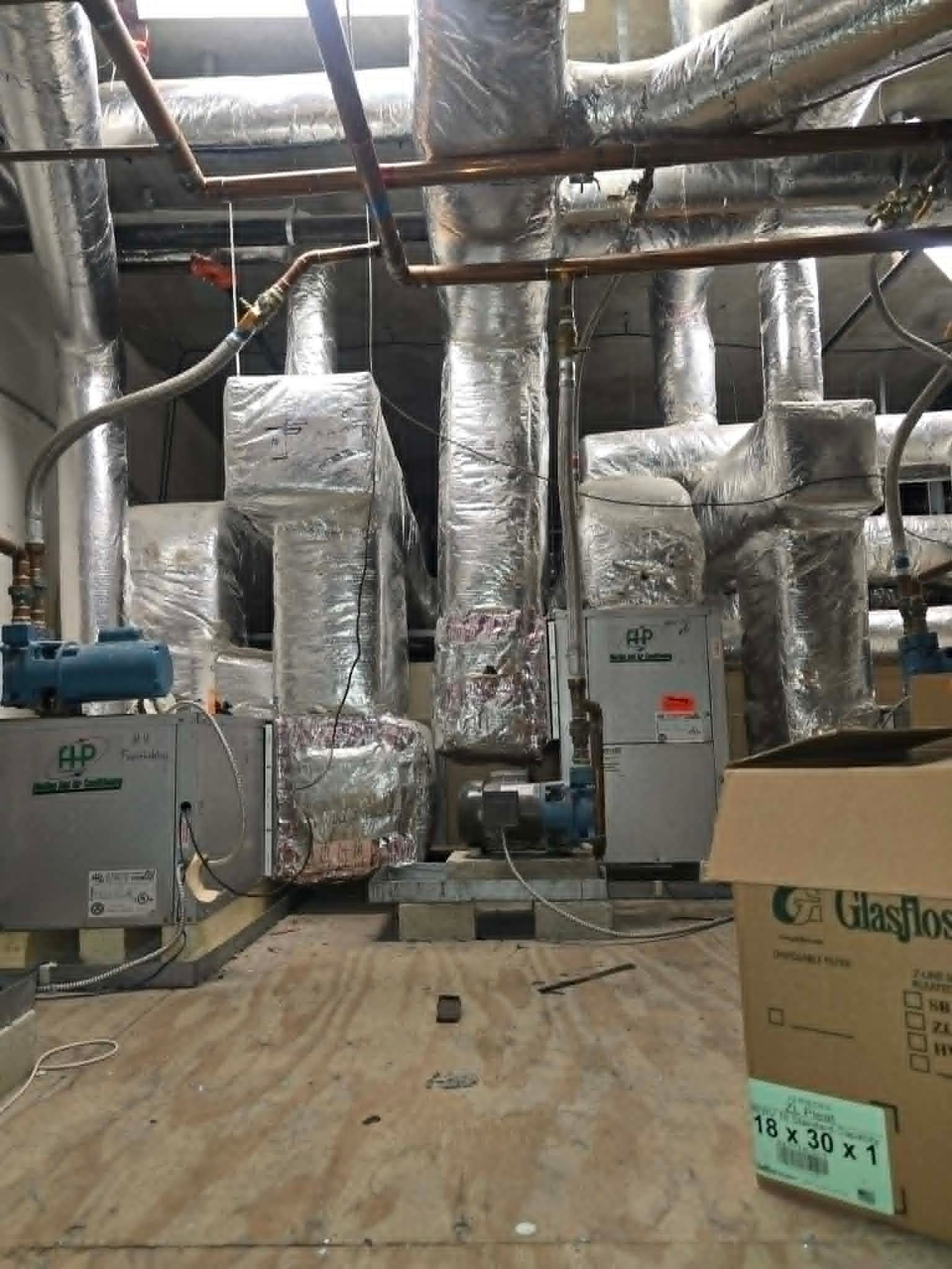 Industrial basement with wrapped ductwork, HVAC units, exposed pipes, and plywood flooring under construction