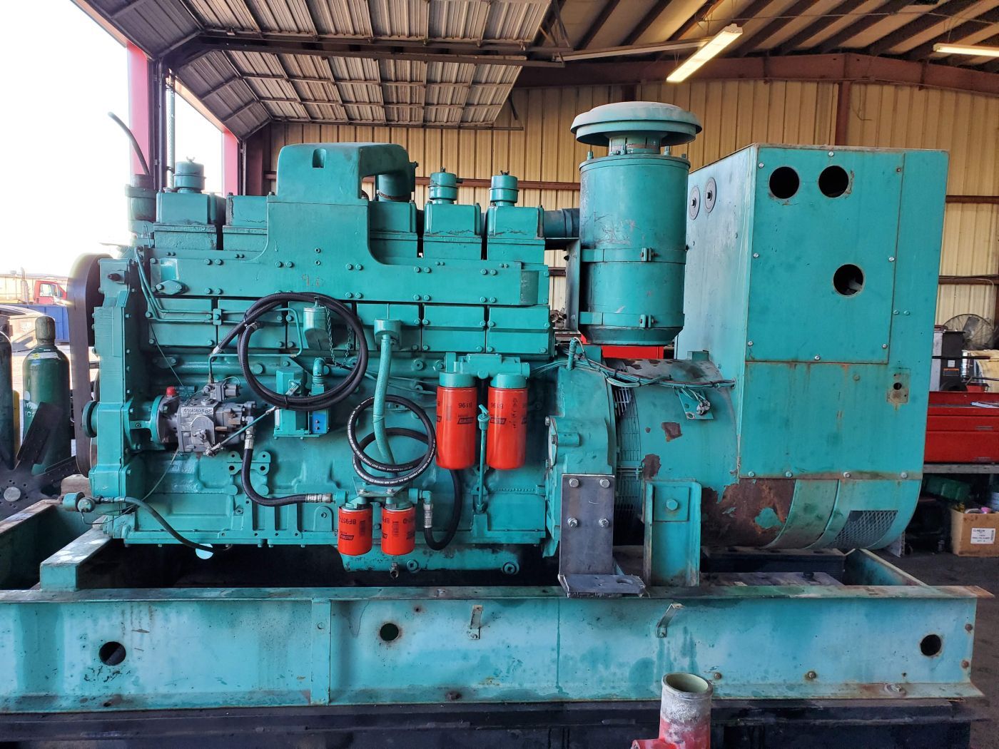 Large turquoise industrial machine on a metal platform inside a warehouse under a roofed shed | S&V Diesel Repair