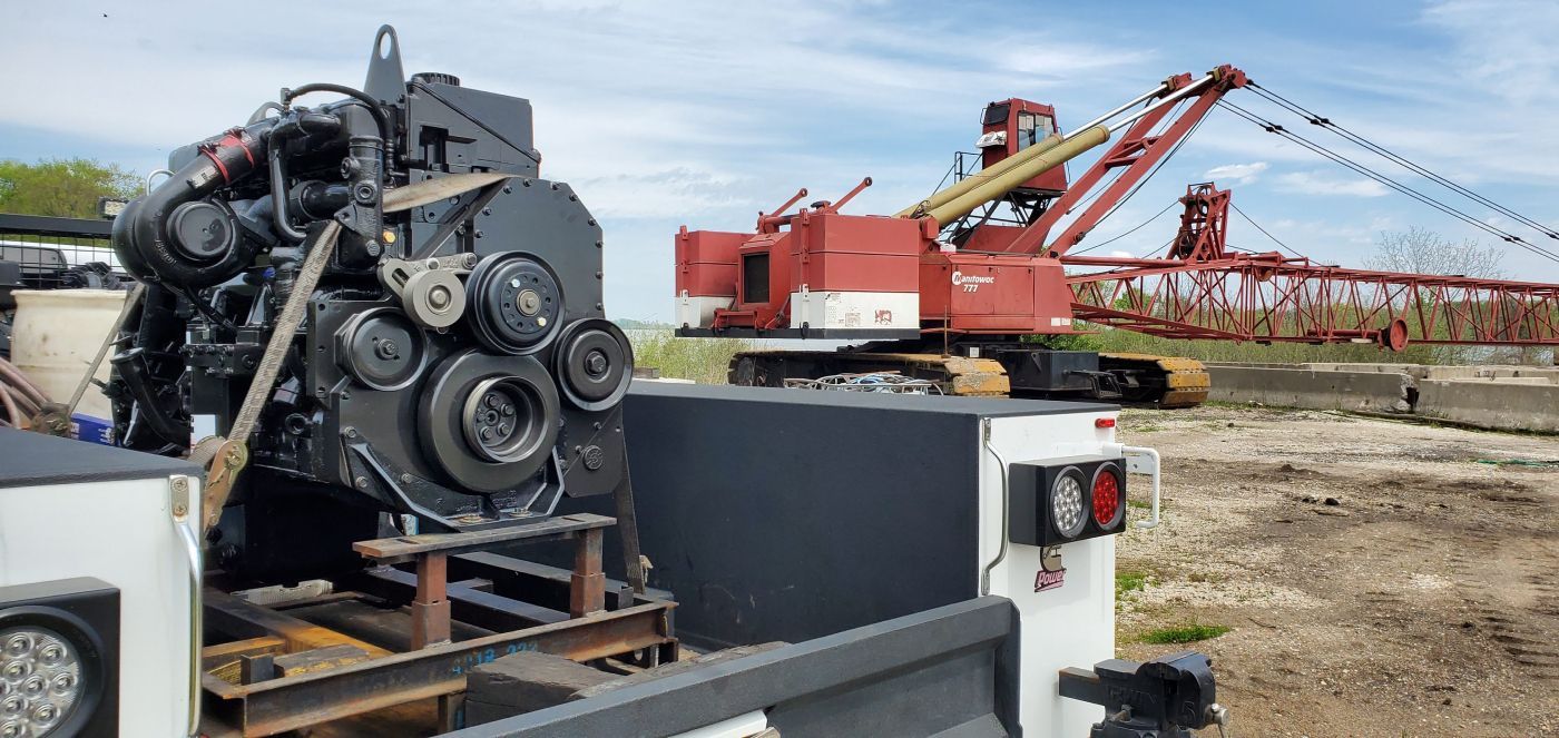 Large black industrial engine on a trailer beside red agricultural machinery in a field | S&V Diesel Repair