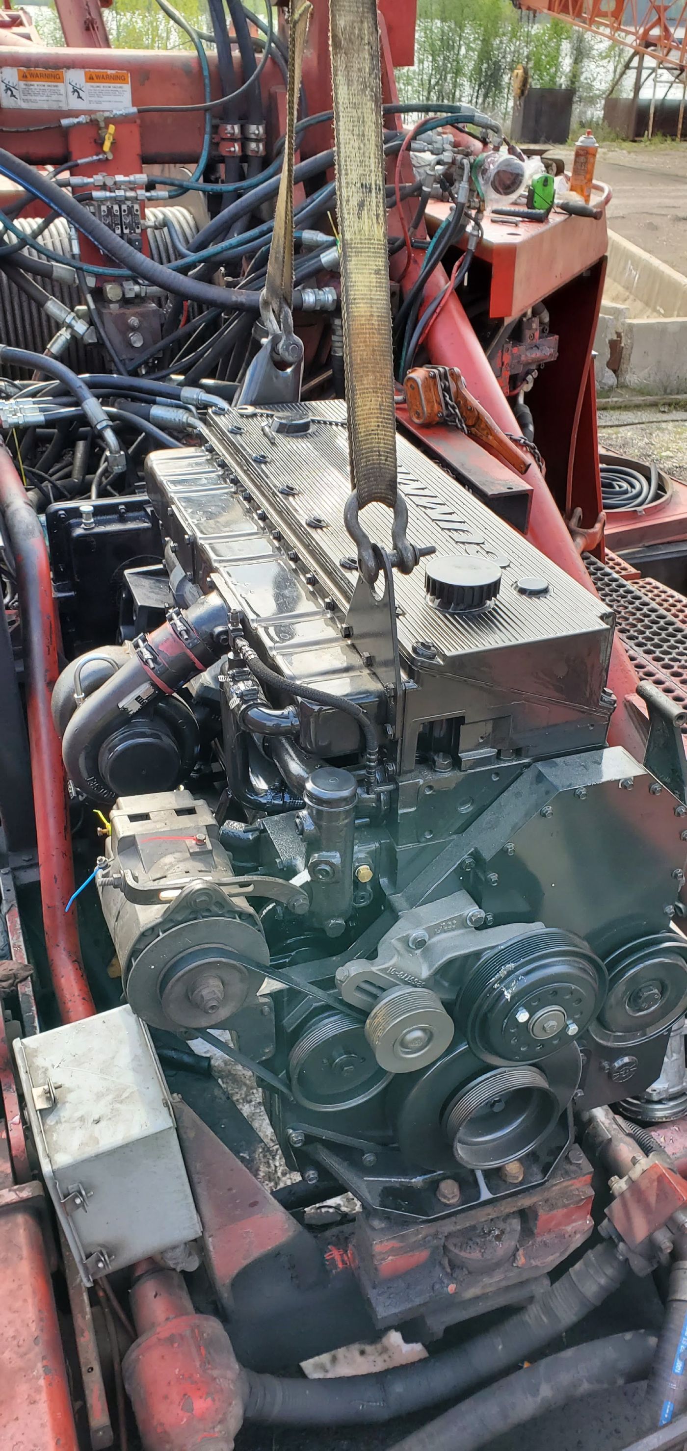 Close-up of a dirty engine block with hoses and metal components on a red machine frame outdoors | S&V Diesel Repair