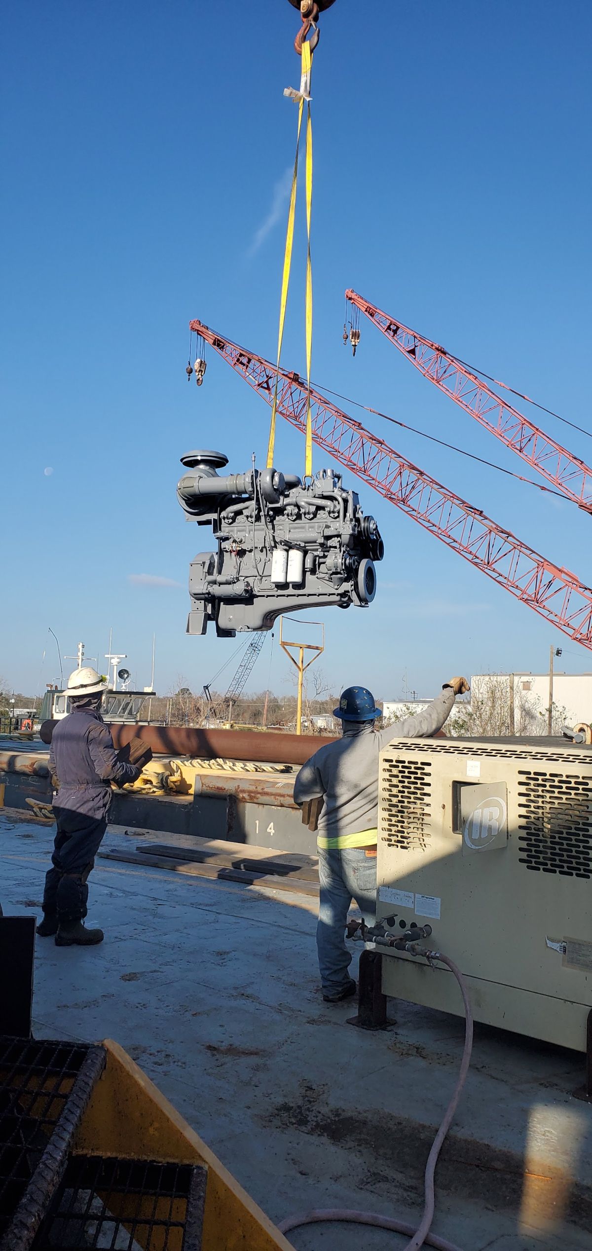 Crane lifting a heavy machine onto a work platform at a construction site under a blue sky | S&V Diesel Repair