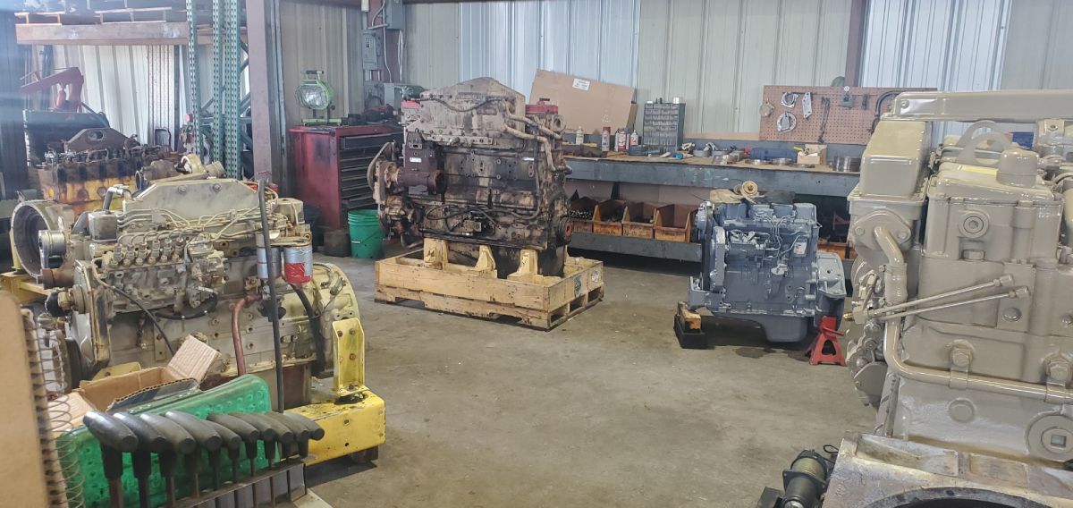 Warehouse with stacked machinery parts and pallets, including a red engine and beige equipment on the floor | S&V Diesel Repair
